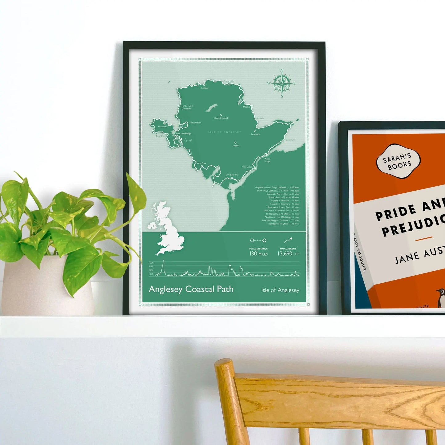 Framed map of Anglesey Coastal Path on a shelf with a plant and book in the background.