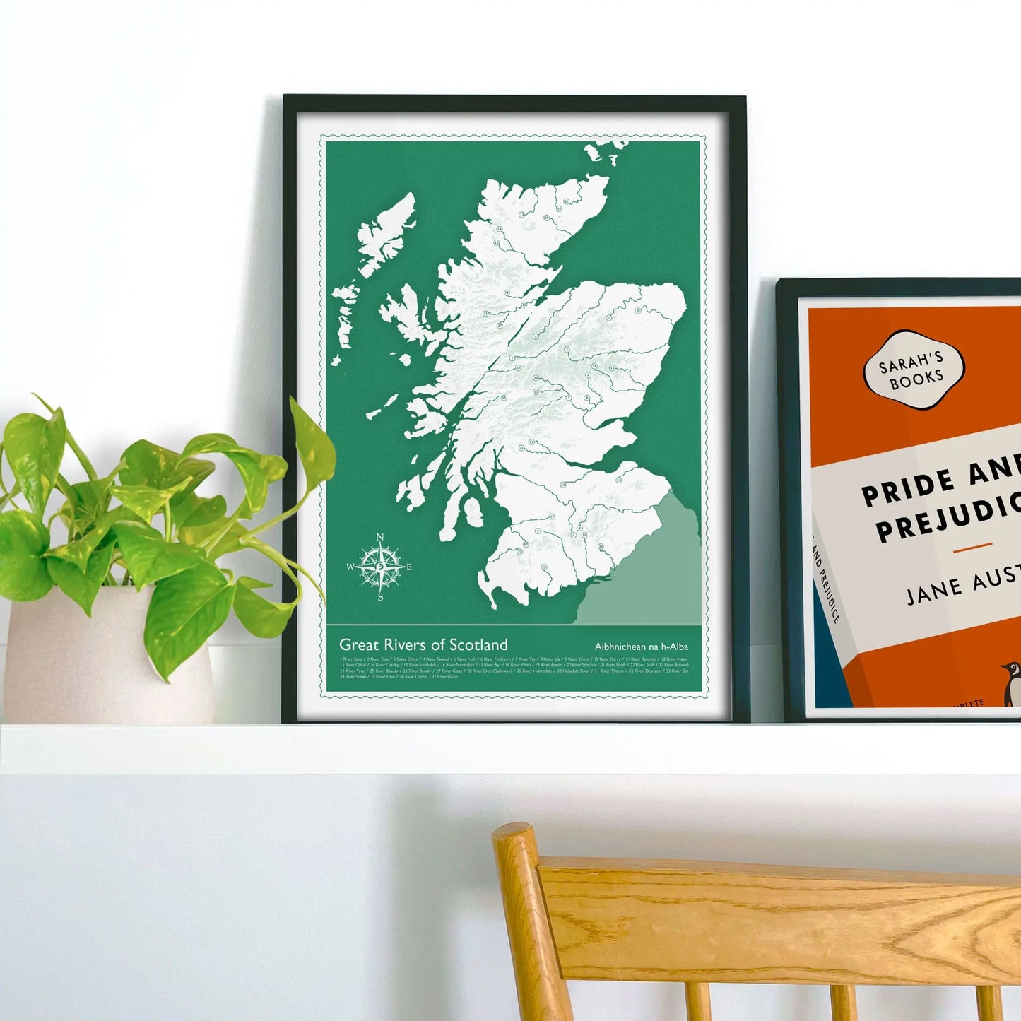 Framed picture on shelf beside a houseplant and another print.