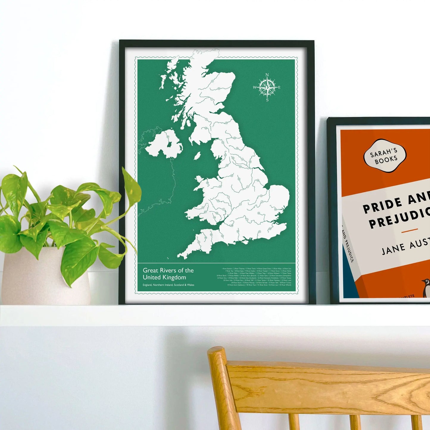 Framed picture on shelf beside a houseplant and another print.