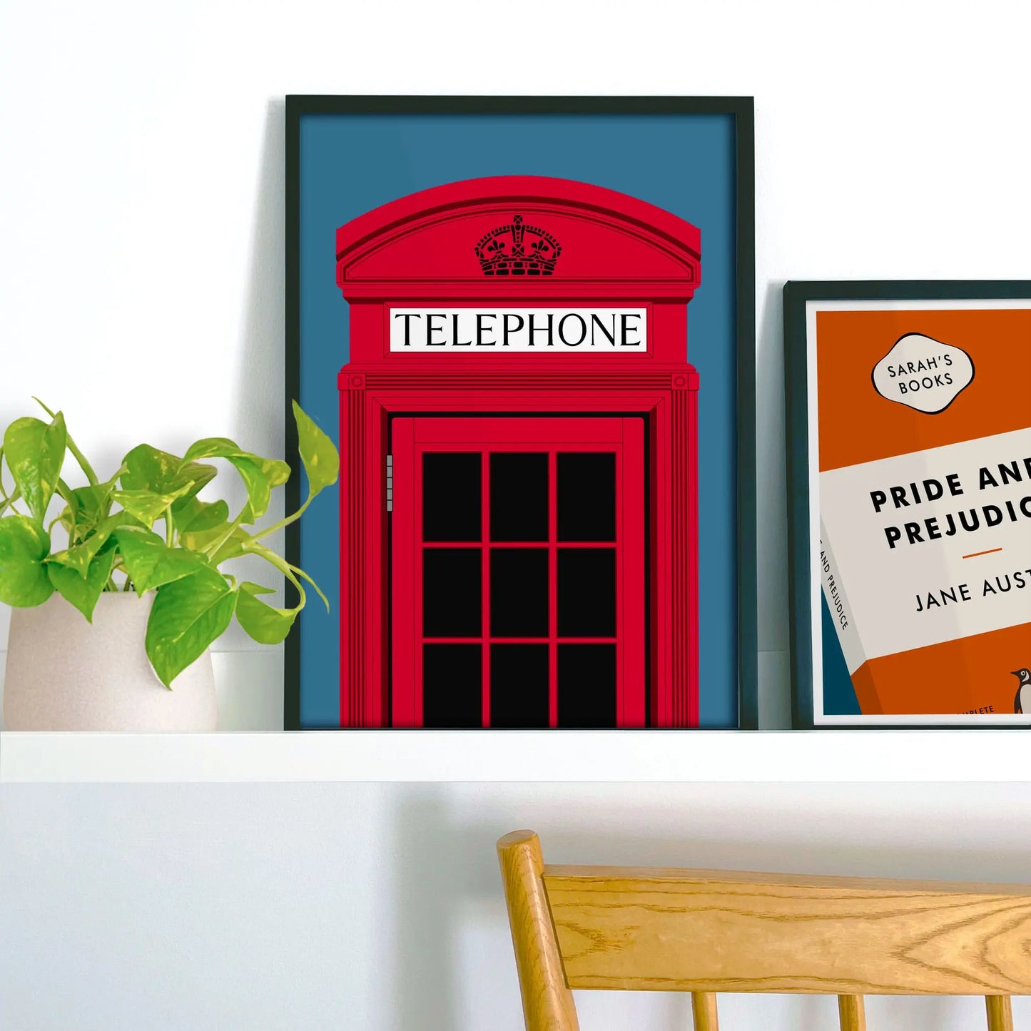 Framed picture on shelf beside a houseplant and another print.