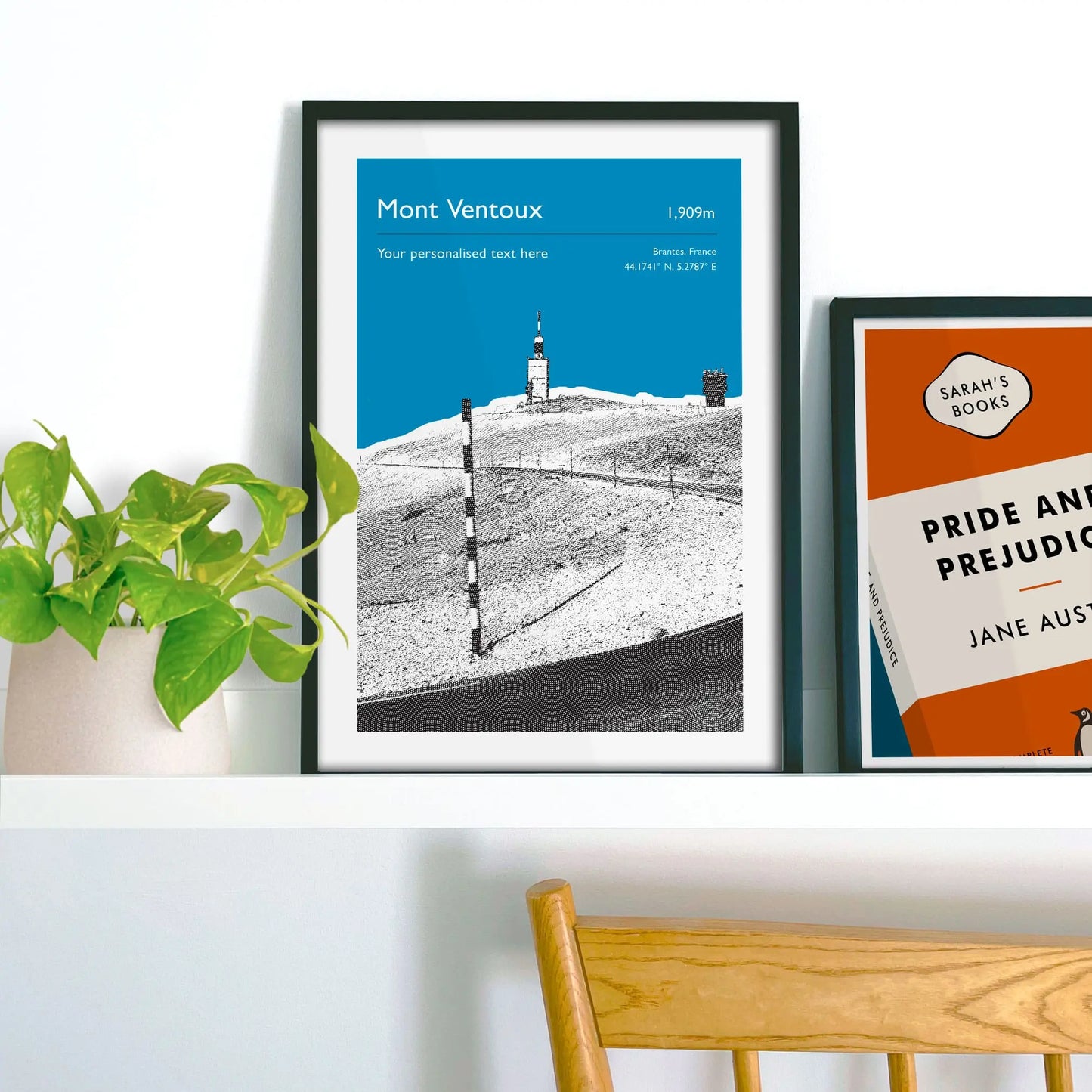 Framed picture on shelf beside a houseplant and another print.