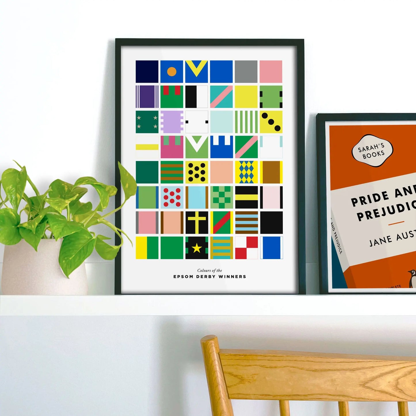 Framed picture on shelf beside a houseplant and another print.
