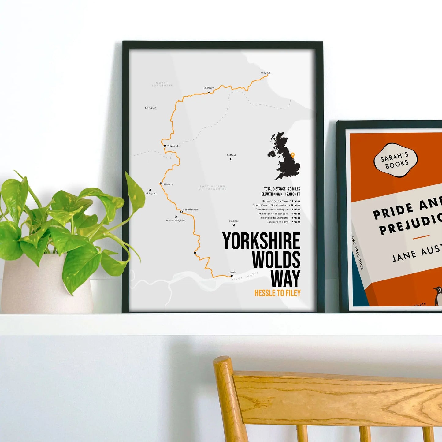 Framed picture on shelf beside a houseplant and another print.