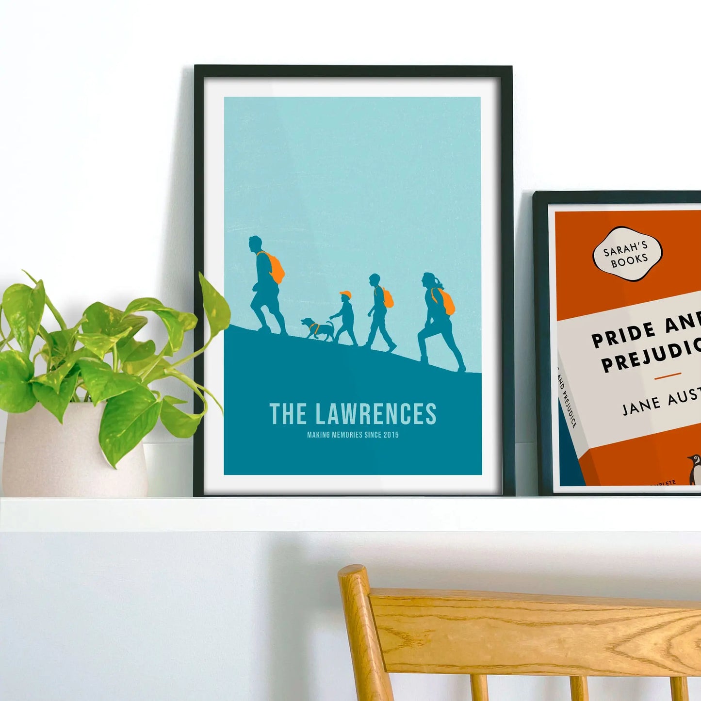 Framed picture on shelf beside a houseplant and another print.
