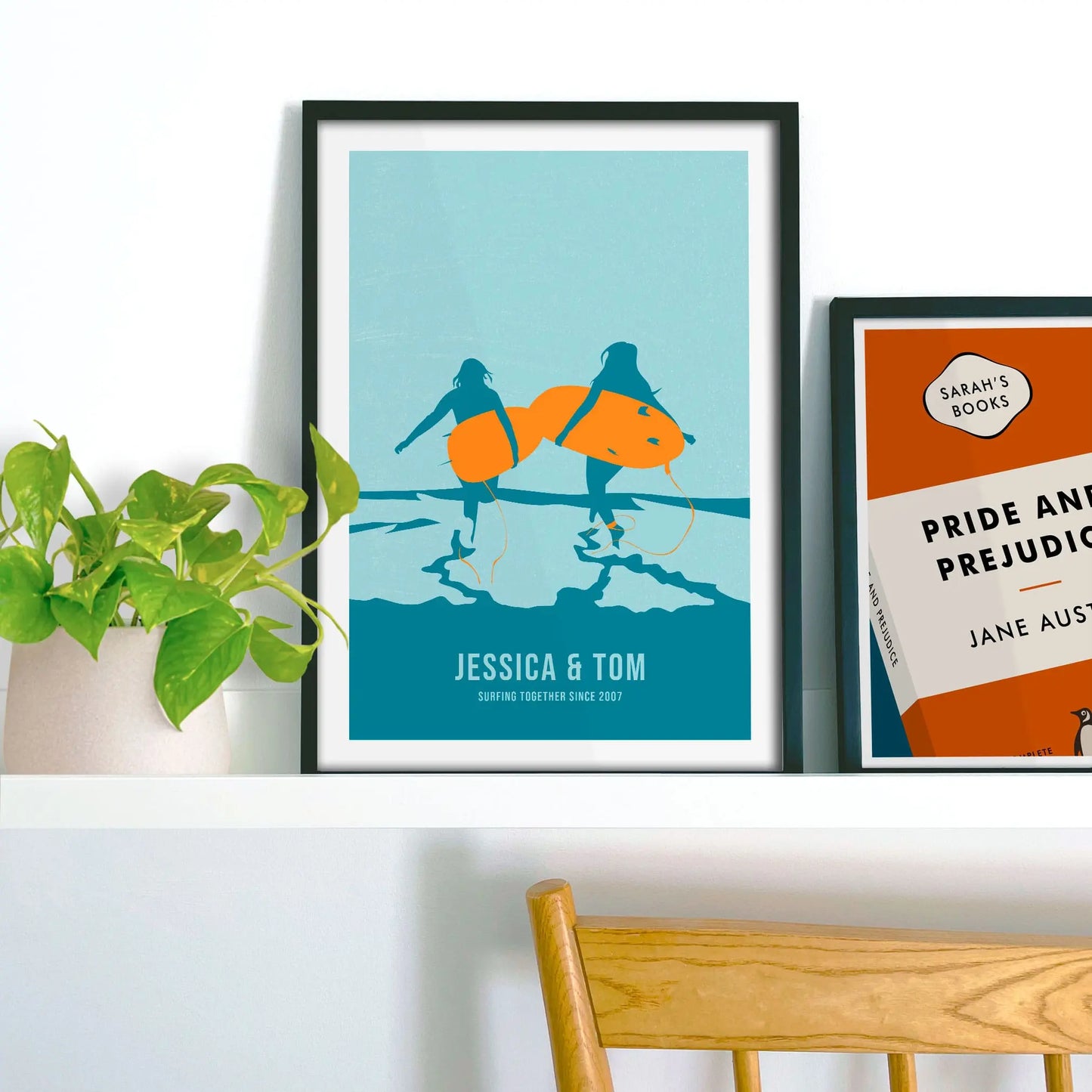 Framed picture on shelf beside a houseplant and another print.