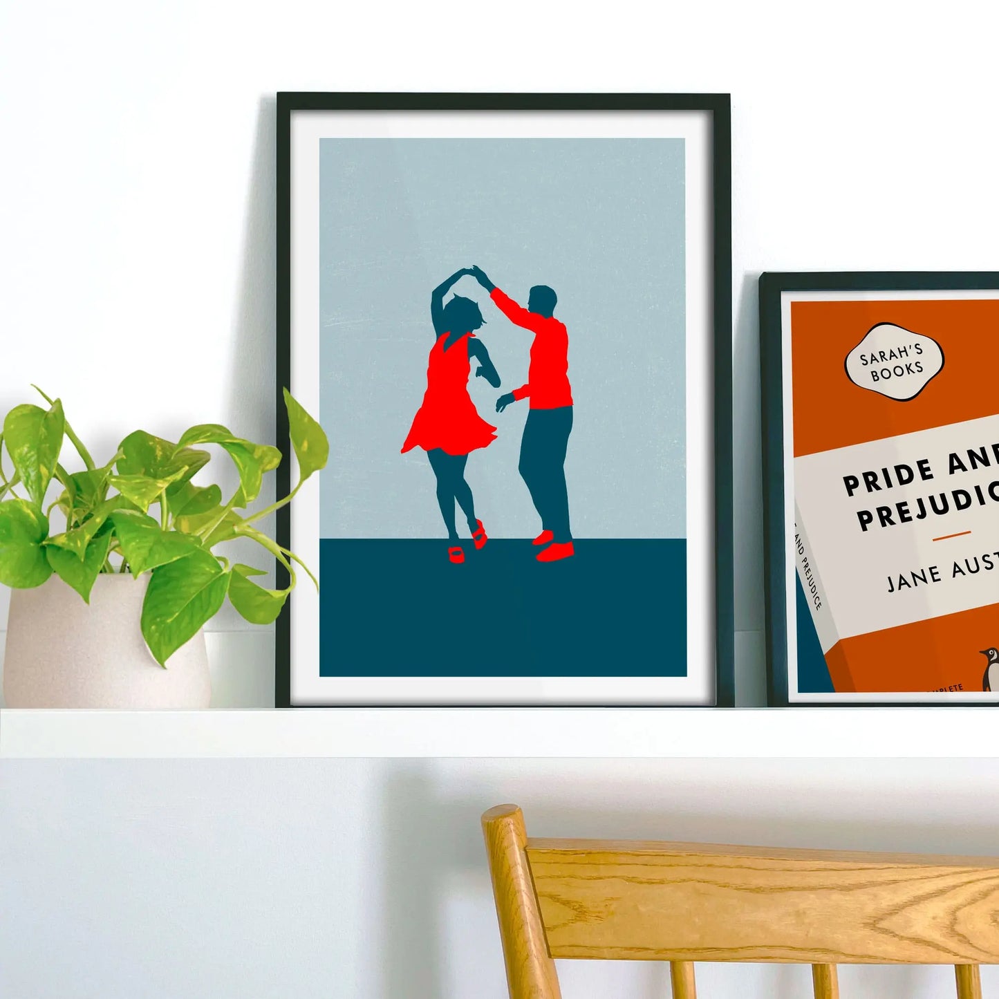 Framed picture on shelf beside a houseplant and another print.