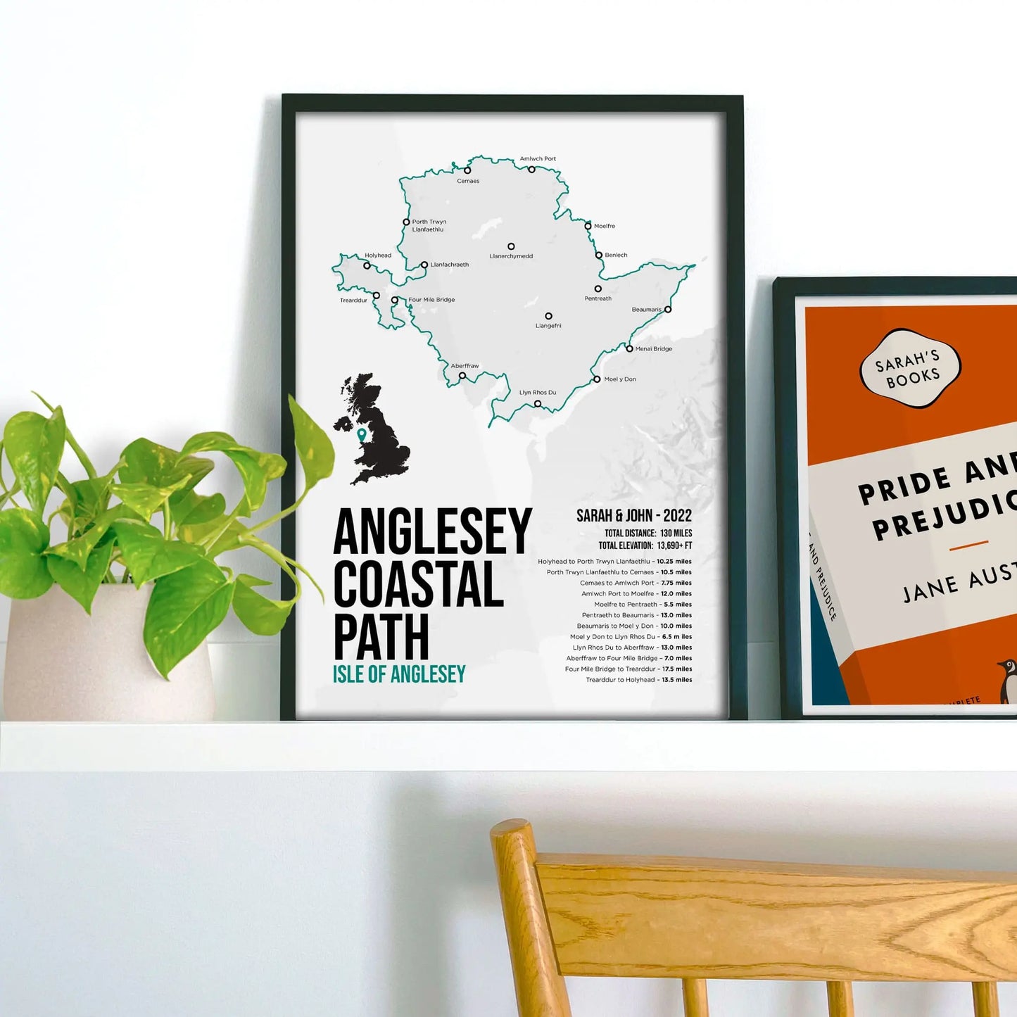 Framed map of Anglesey Coastal Path on a shelf with a plant and book.