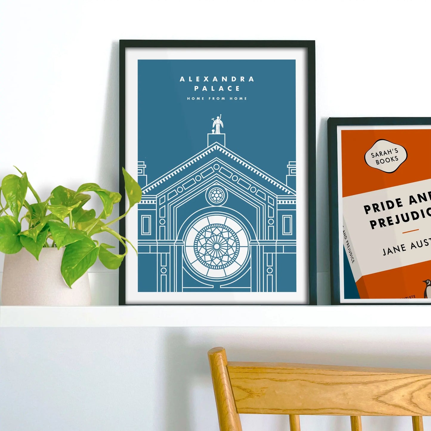 Framed picture on shelf beside a houseplant and another print.