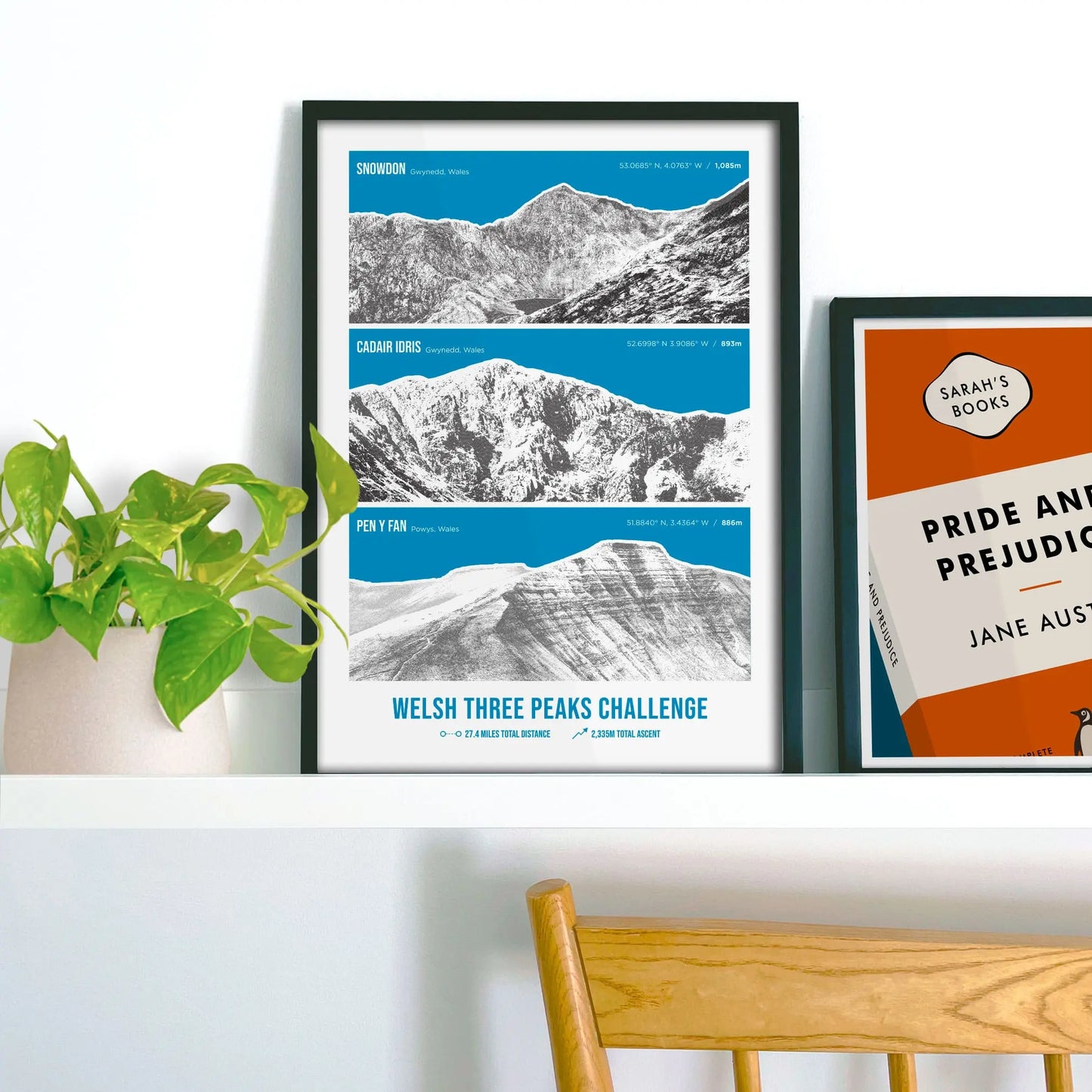 Framed print on shelf beside houseplant and another framed picture.