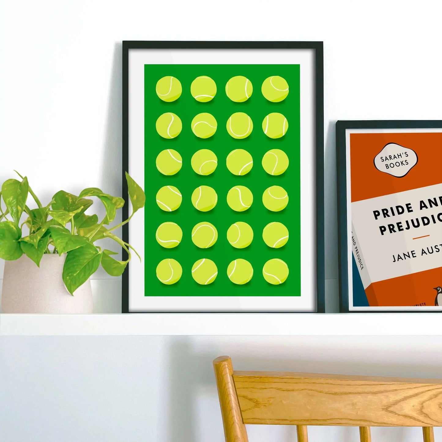 Framed picture on shelf beside a houseplant and another print.