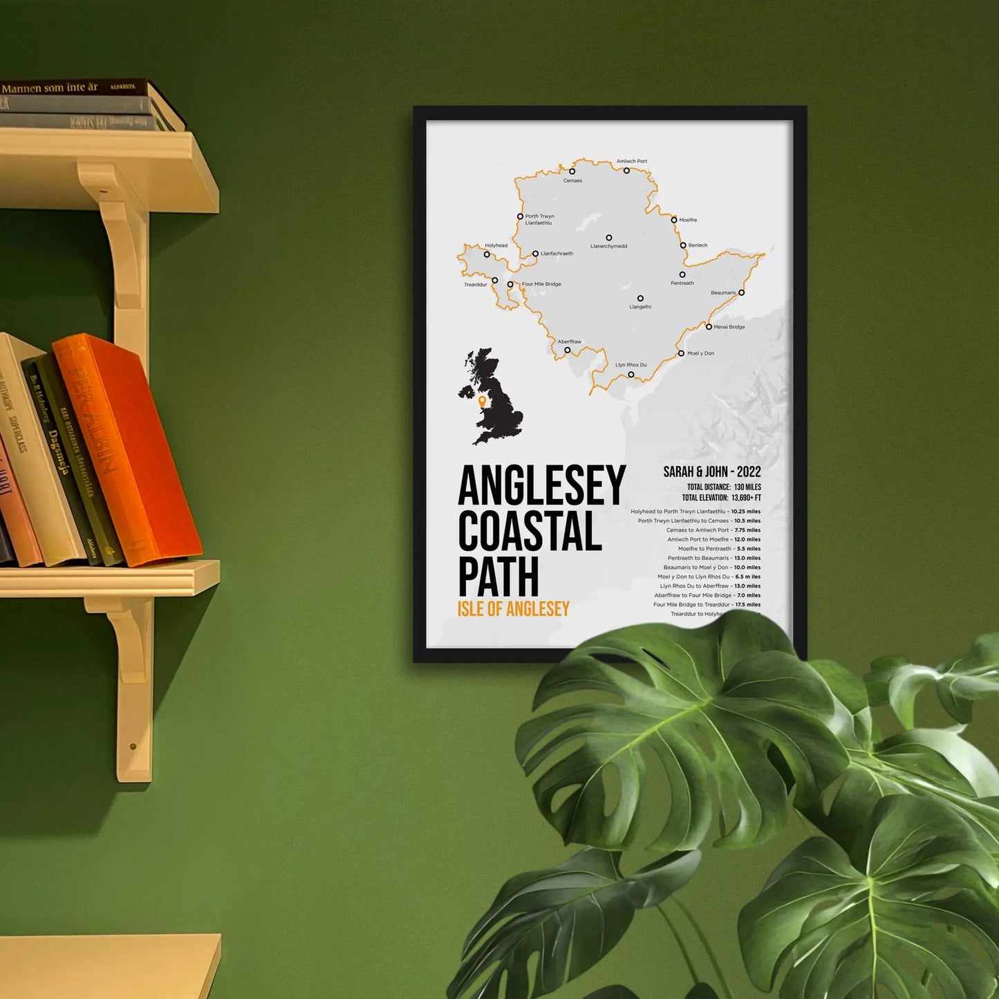 Framed map of Anglesey Coastal Path on a green wall with books and a plant.