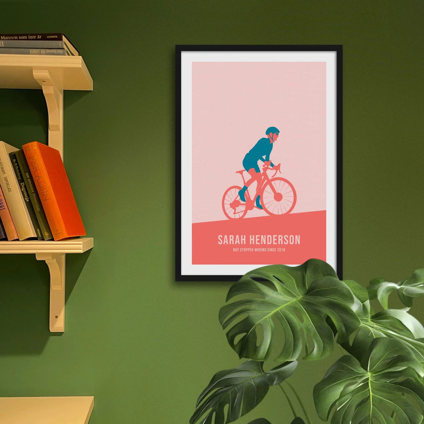 Framed print on green wall beside shelves behind houseplant.