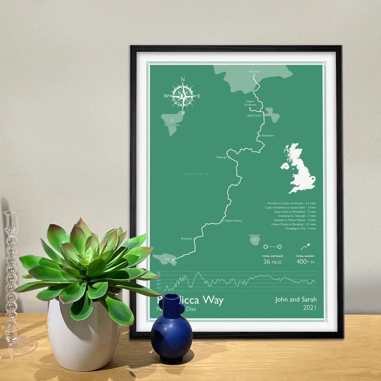 Framed print on sideboard beside plant and candlestick