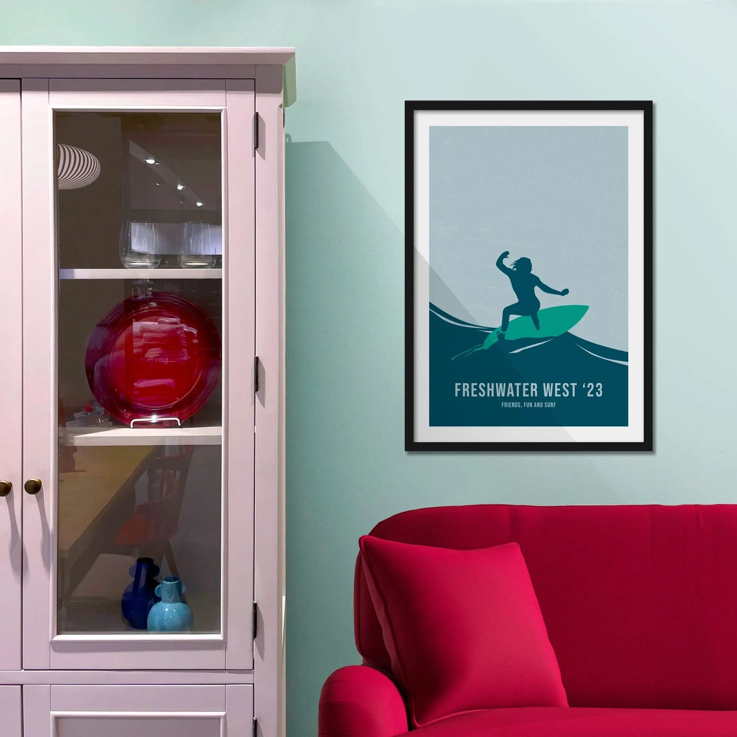 Framed picture on a baby blue wall beside pink shelving