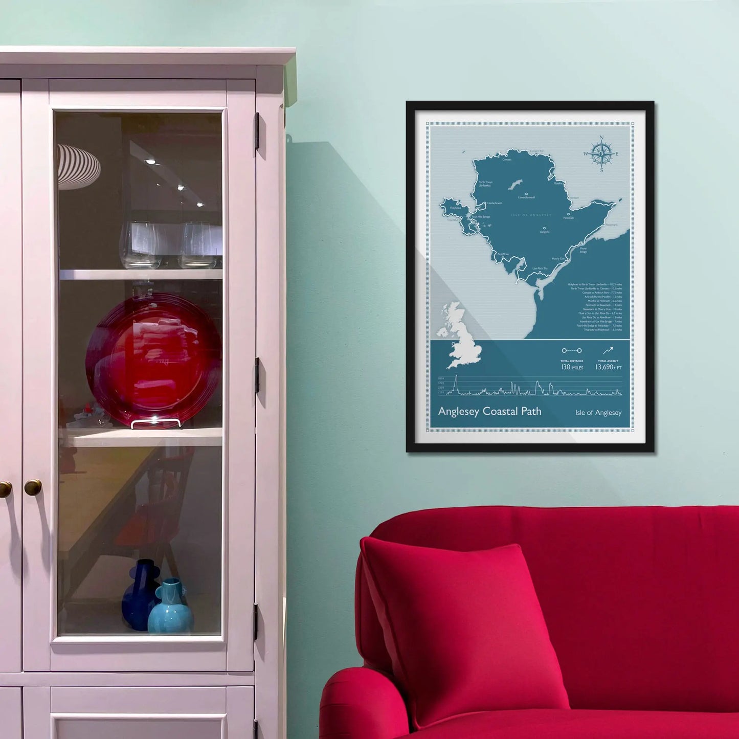 Framed map of Anglesey Coastal Path on a light blue wall above a red sofa.