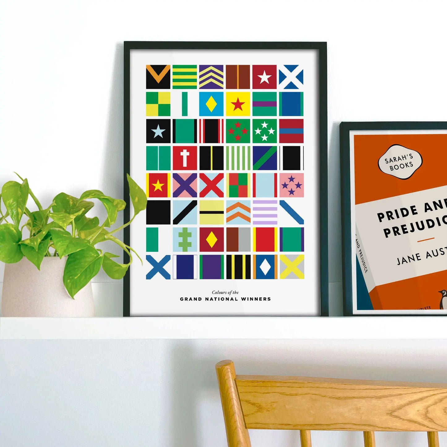 Framed poster with colorful geometric design on a shelf with a plant and book.