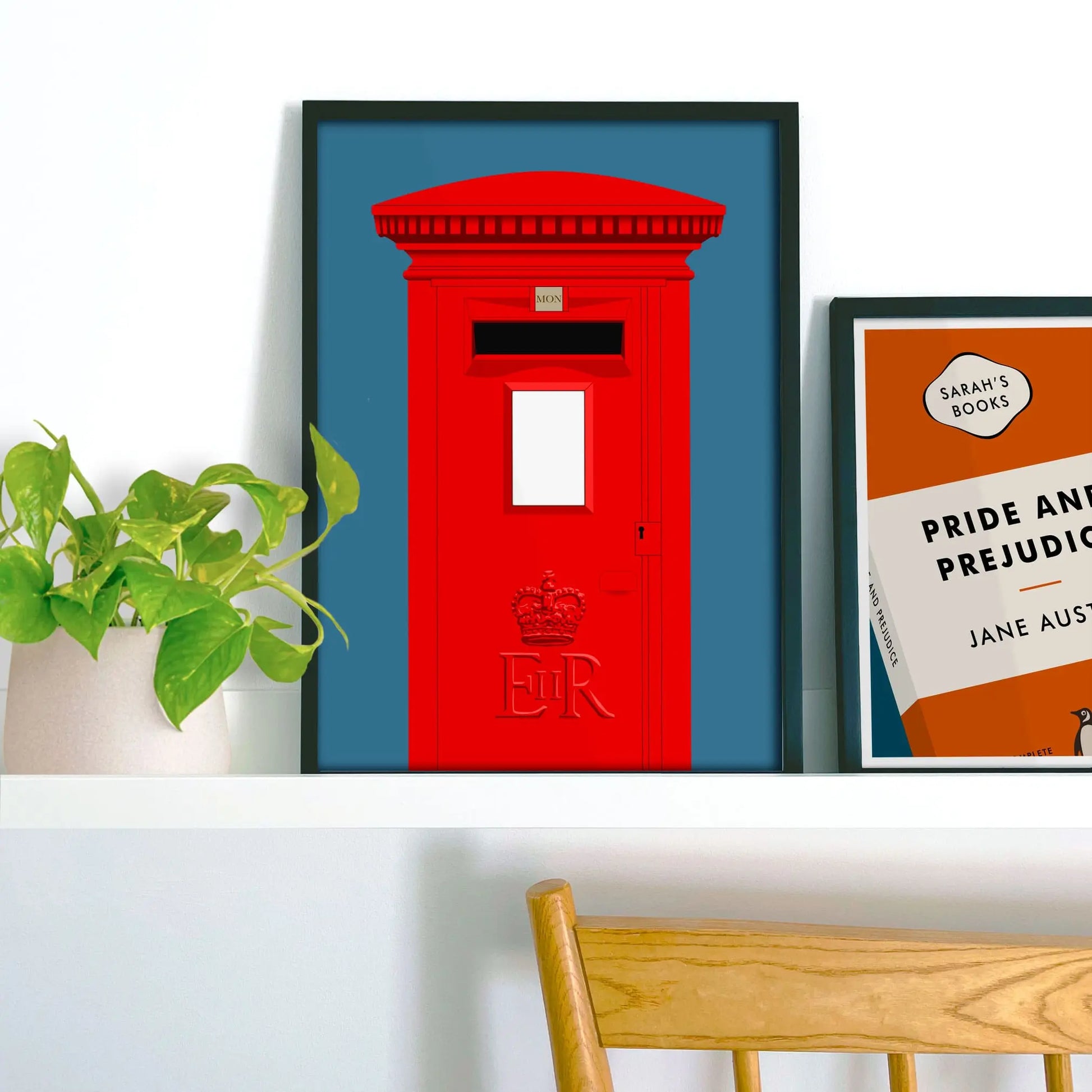 Framed picture on shelf beside a houseplant and another print.