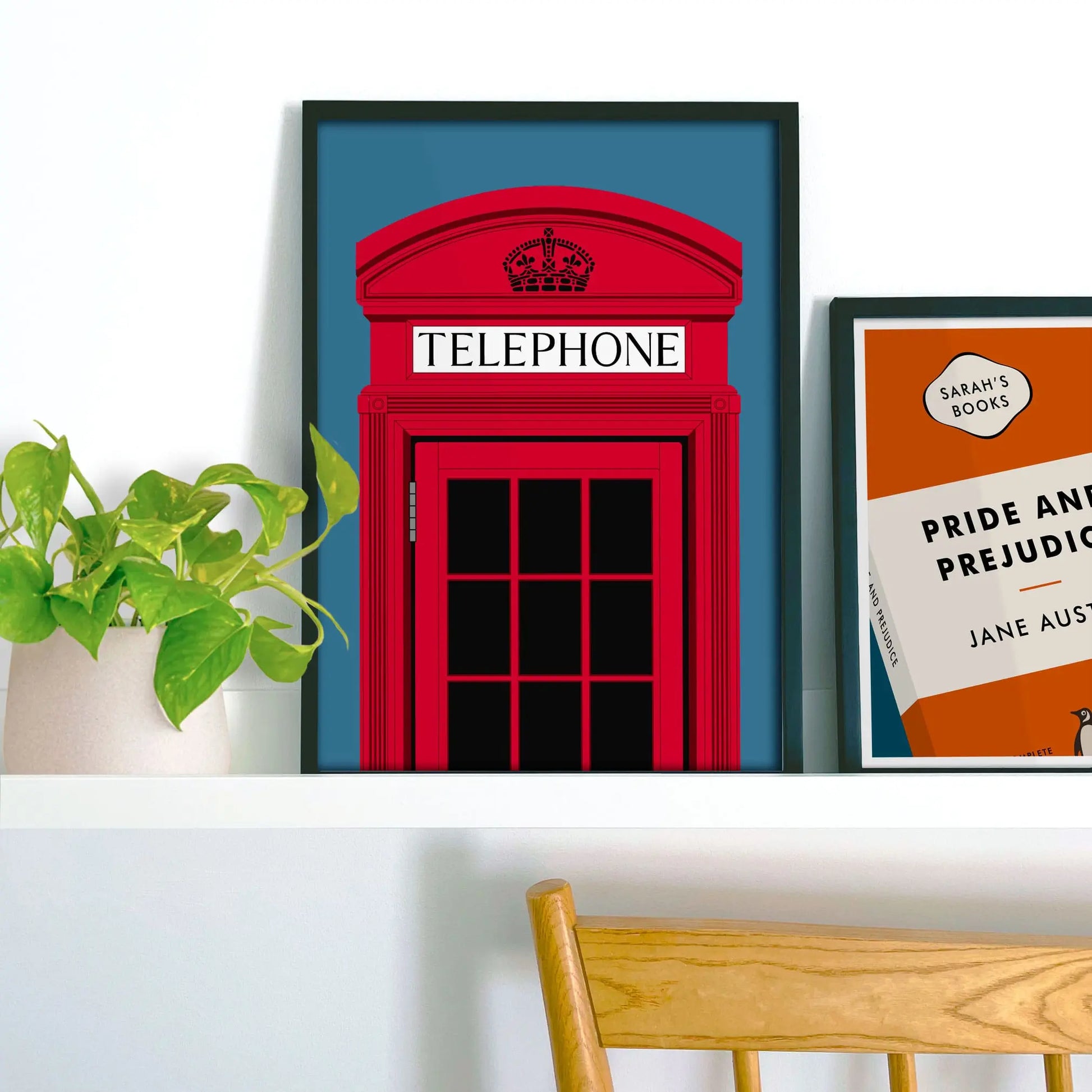 Framed picture on shelf beside a houseplant and another print.