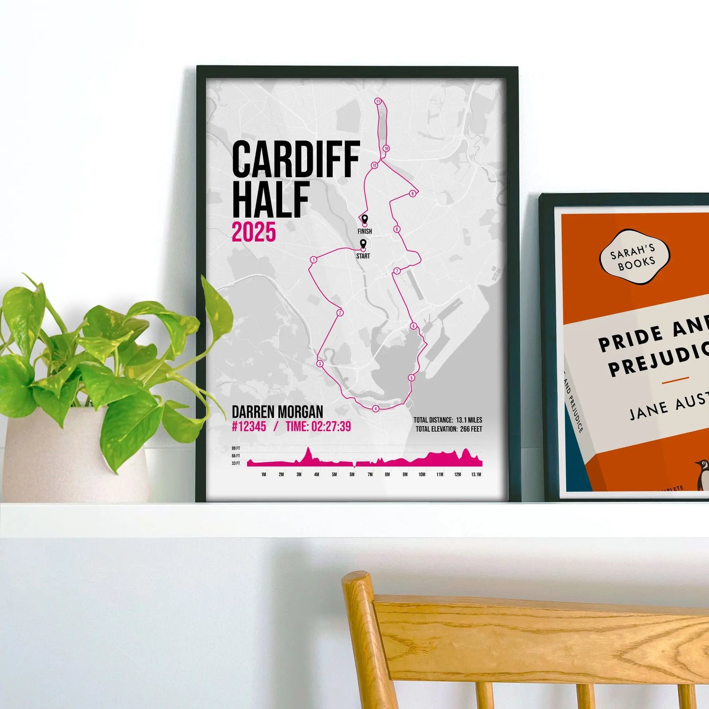 Framed print on shelf beside another print and a houseplant