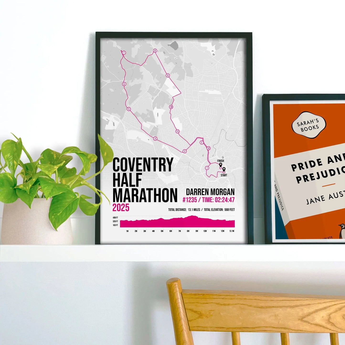 Framed pink print on a shelf beside a houseplant and another print