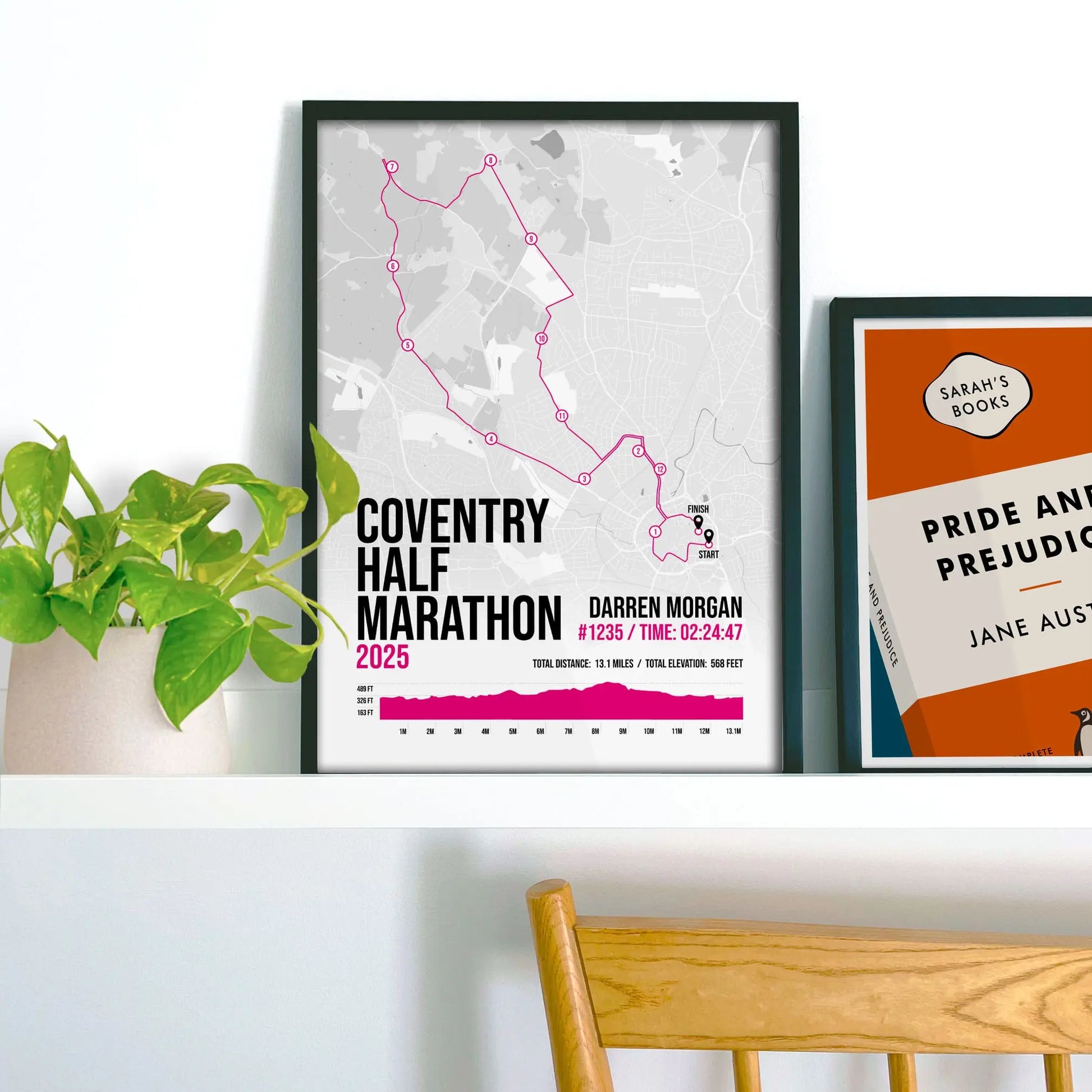 Framed pink print on a shelf beside a houseplant and another print