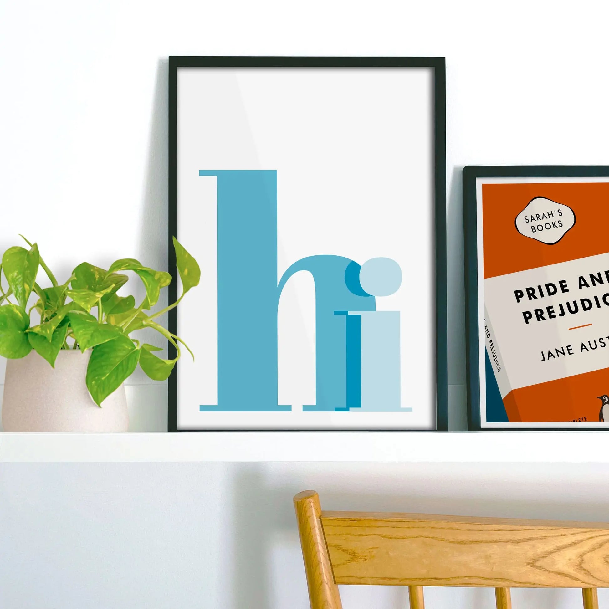 Framed picture on shelf beside a houseplant and another print.