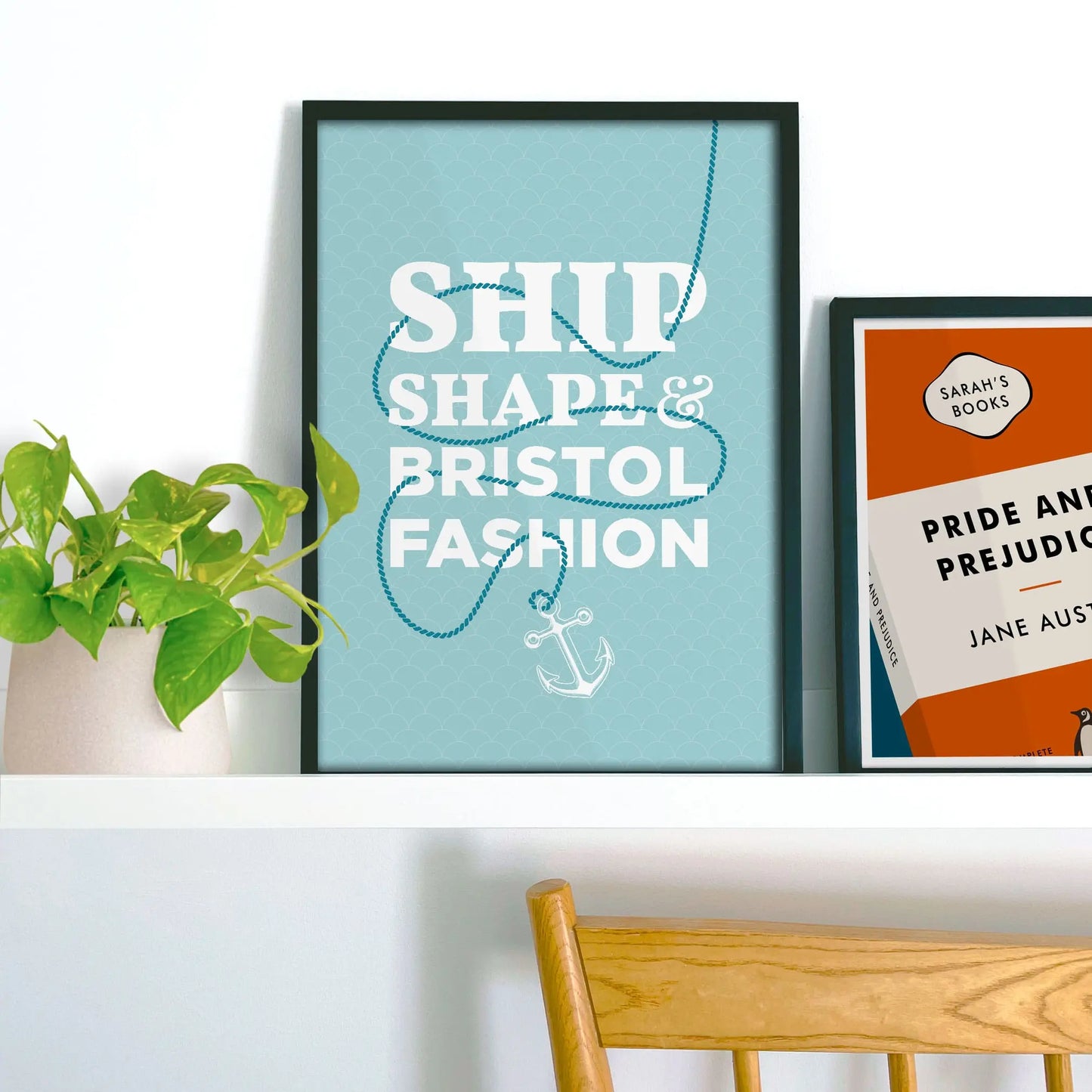 Framed picture on shelf beside a houseplant and another print.