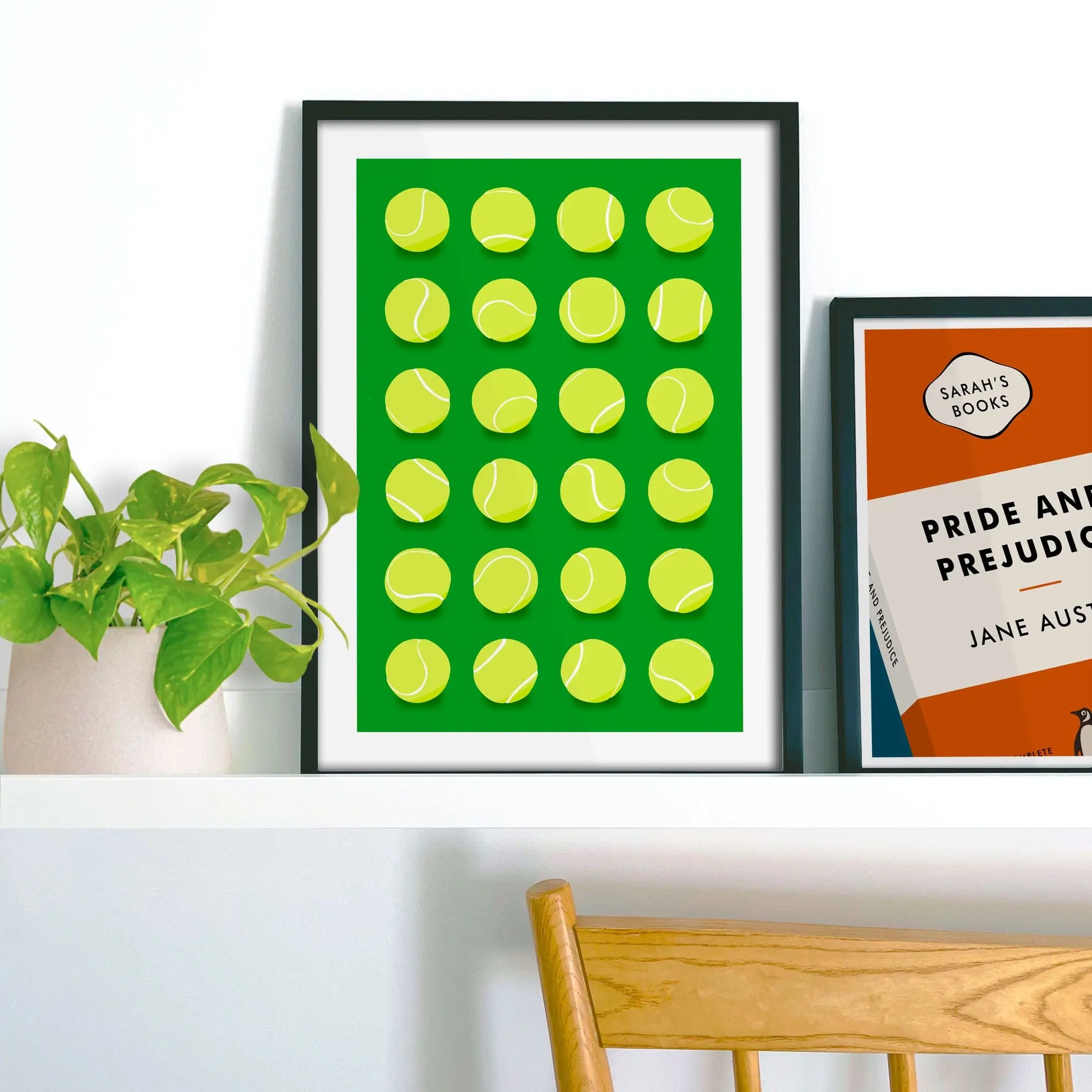 Framed picture on shelf beside a houseplant and another print.