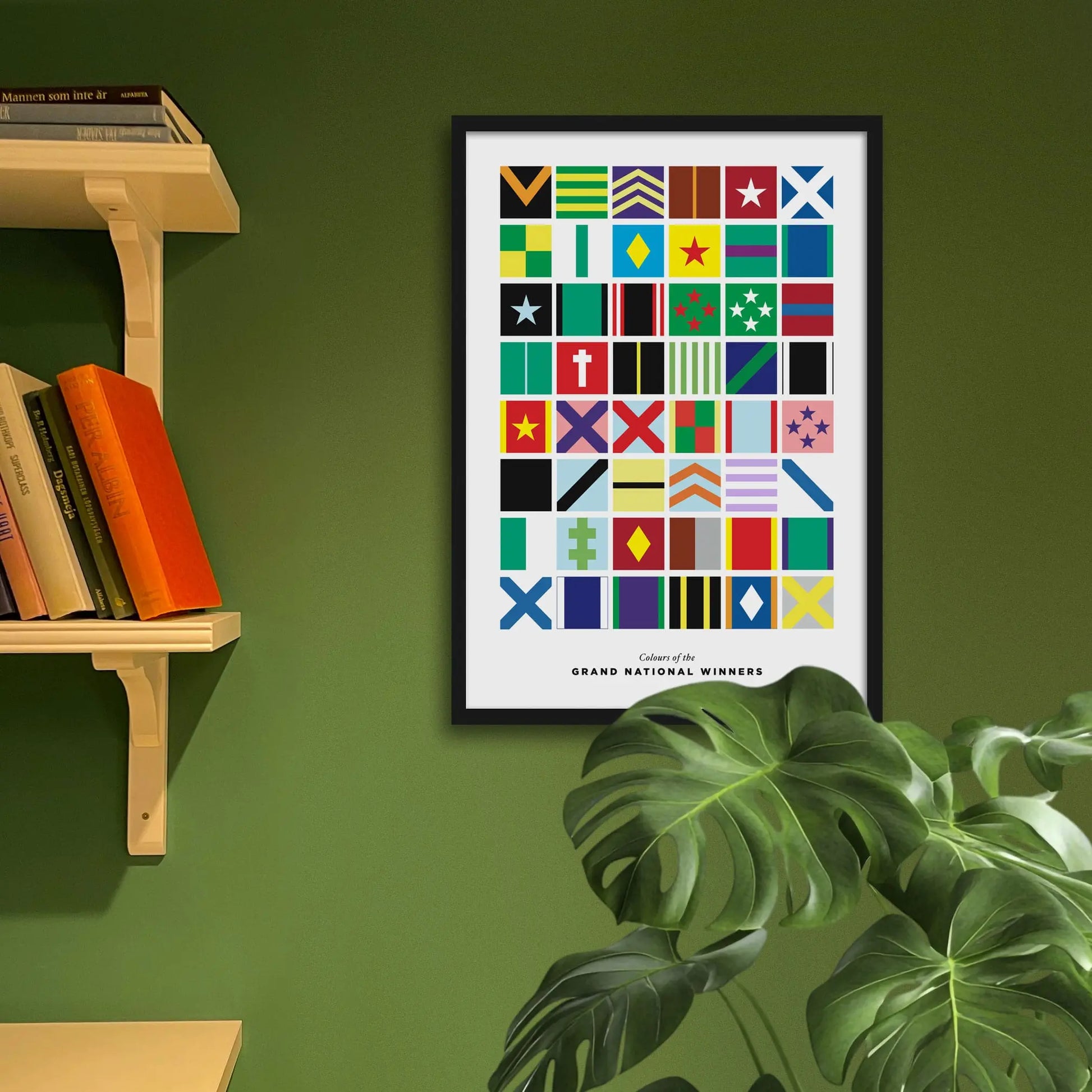 Framed poster with colorful geometric design on a green wall with a bookshelf and plant.