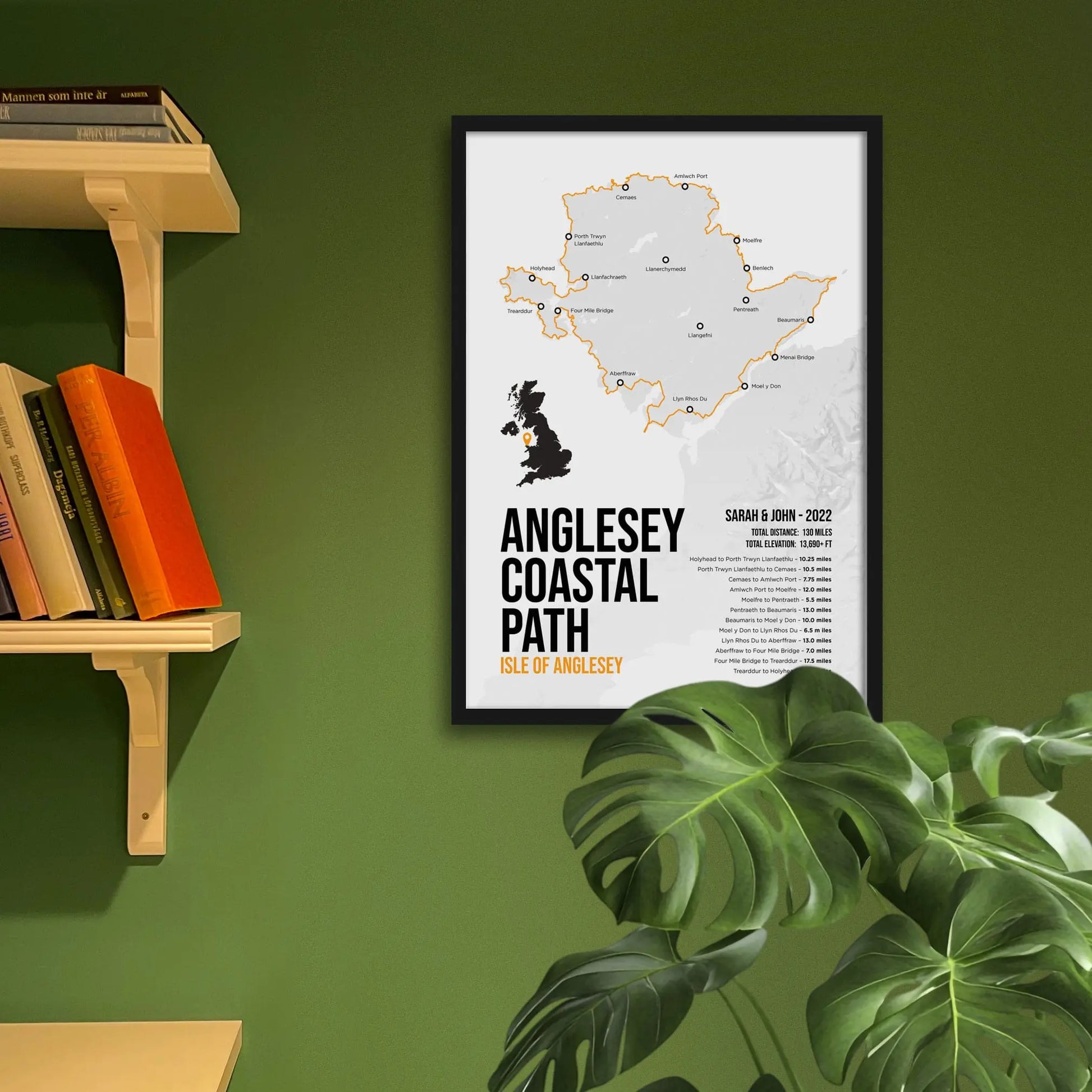 Framed map of Anglesey Coastal Path on a green wall with books and a plant.