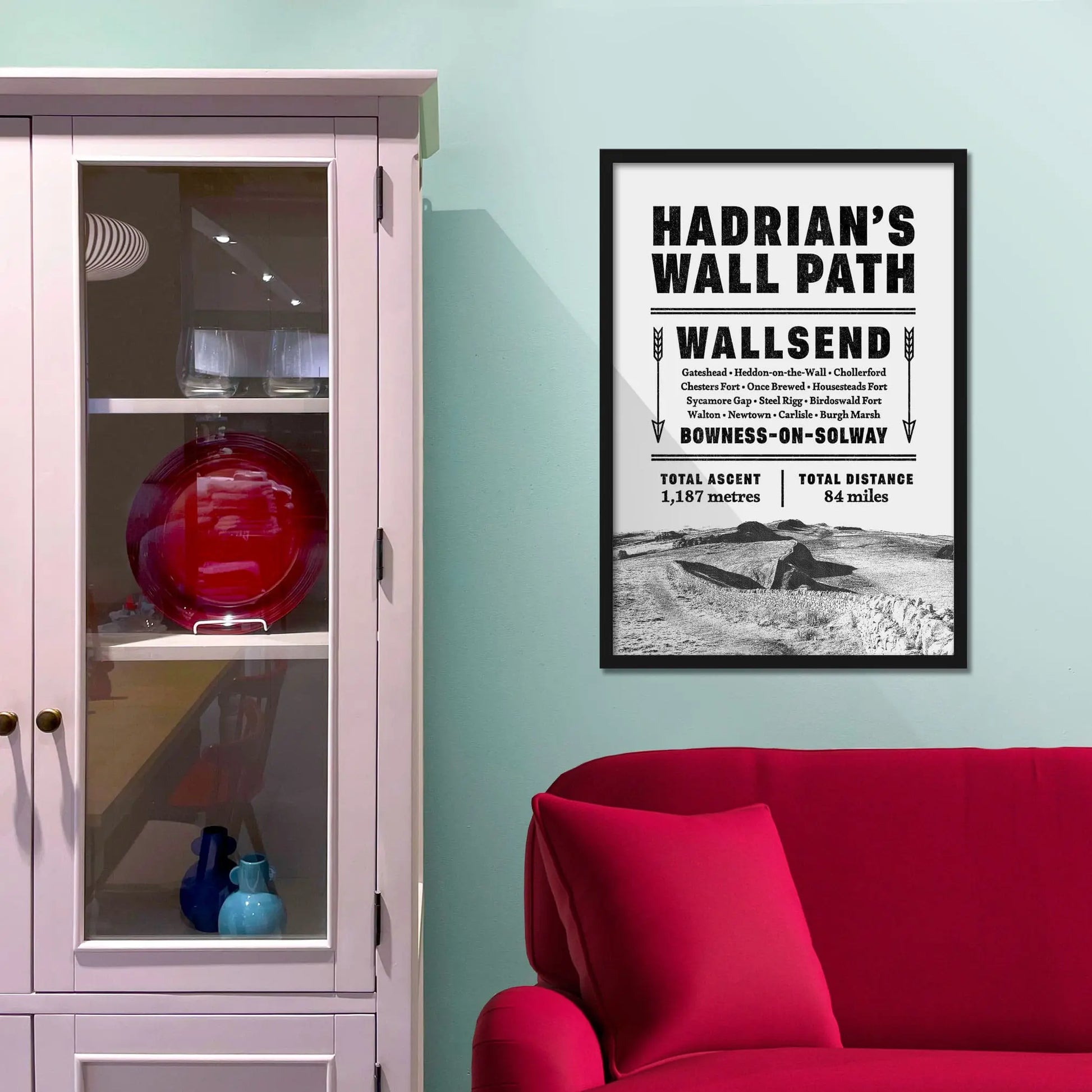 Framed picture on a baby blue wall beside pink shelving