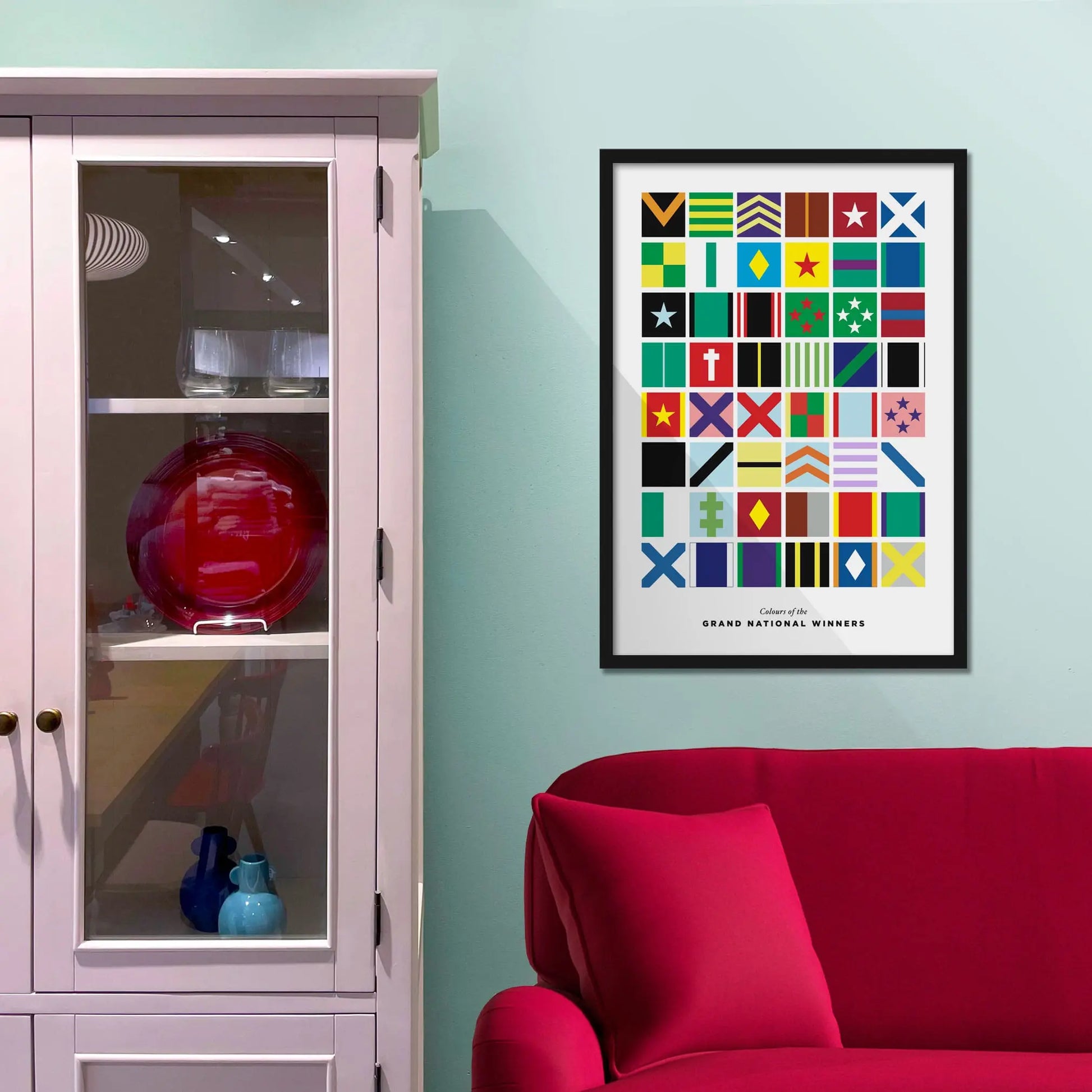 Framed colorful geometric art print on a light blue wall above a red sofa.
