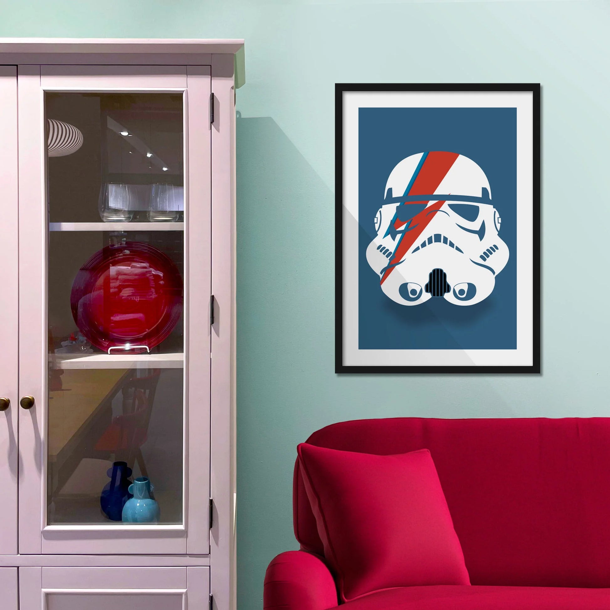 Framed picture on blue wall beside shelves above a red sofa