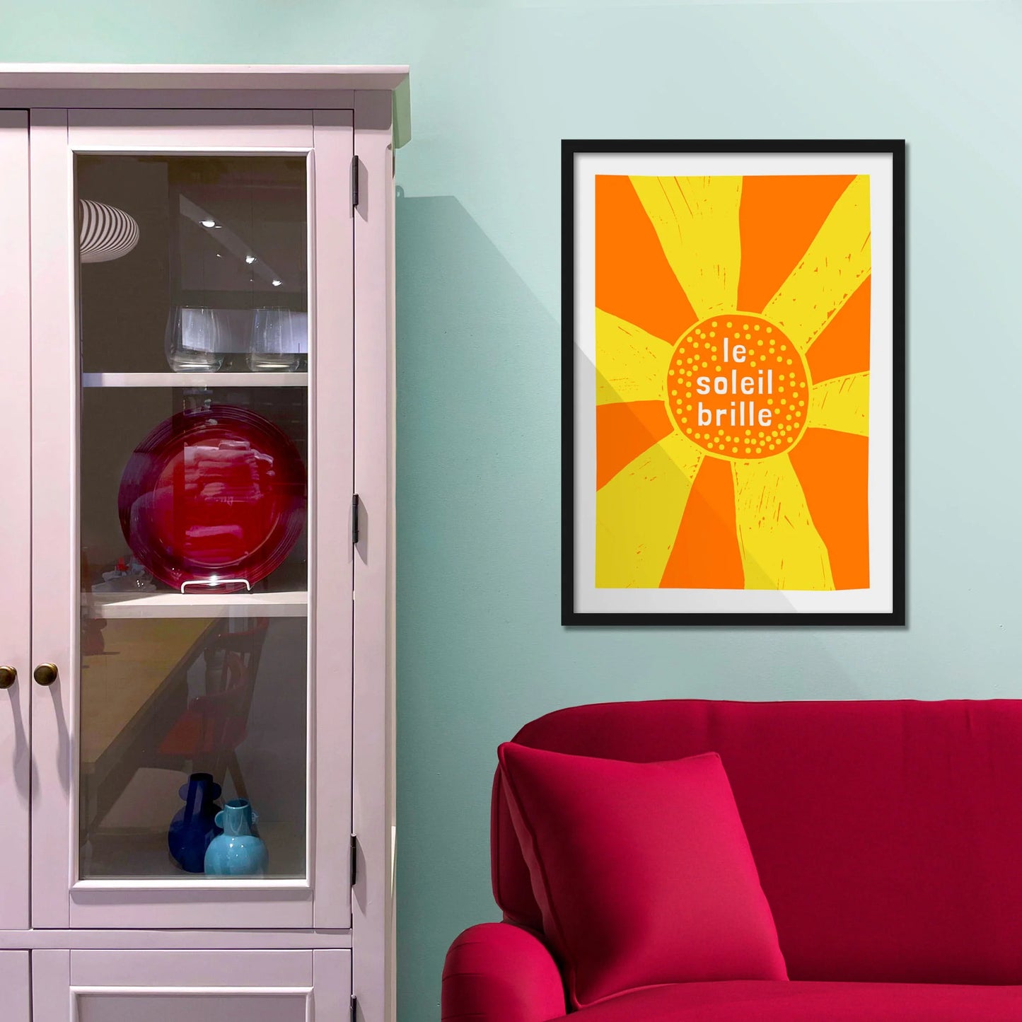 Framed picture on blue wall beside shelves above a red sofa