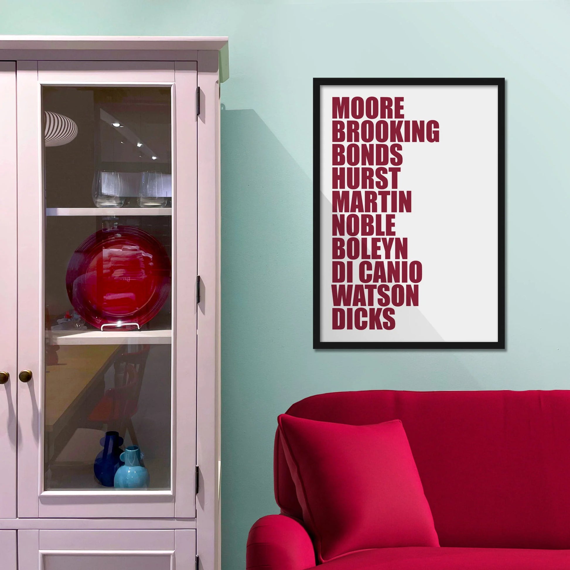 Framed picture on blue wall beside shelves above a red sofa