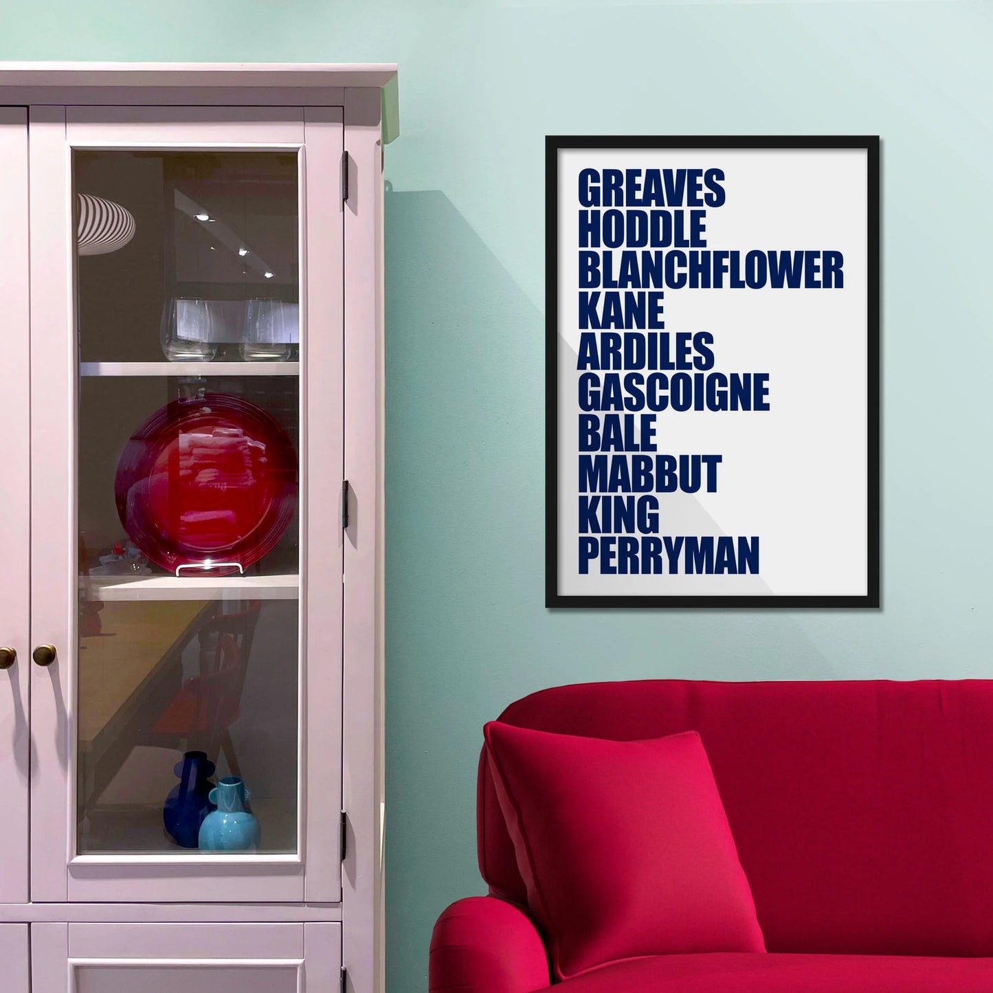 Framed picture on blue wall beside shelves above a red sofa