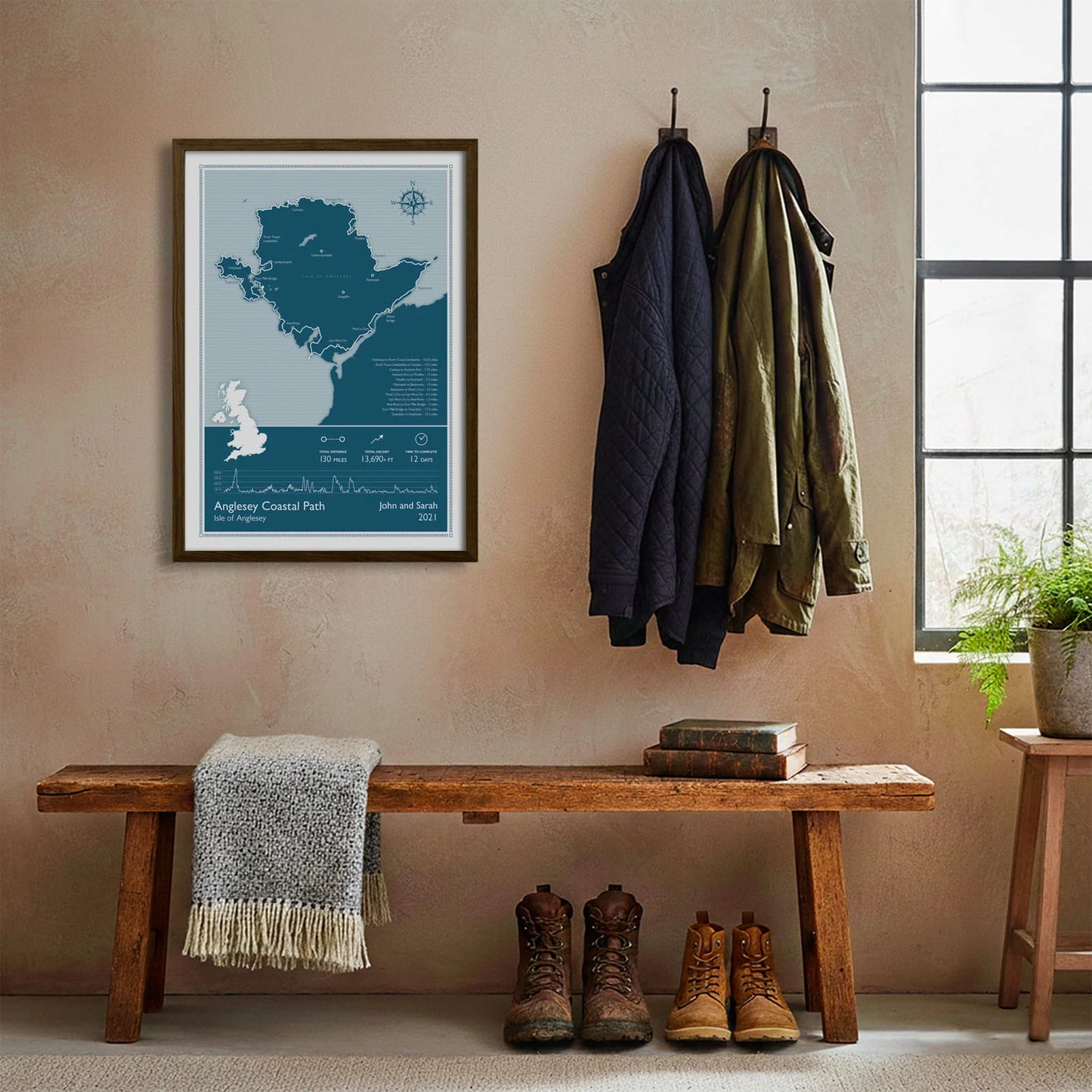 Framed print hanging on cream wall beside coats hanging above bench with walking boots and a scarf