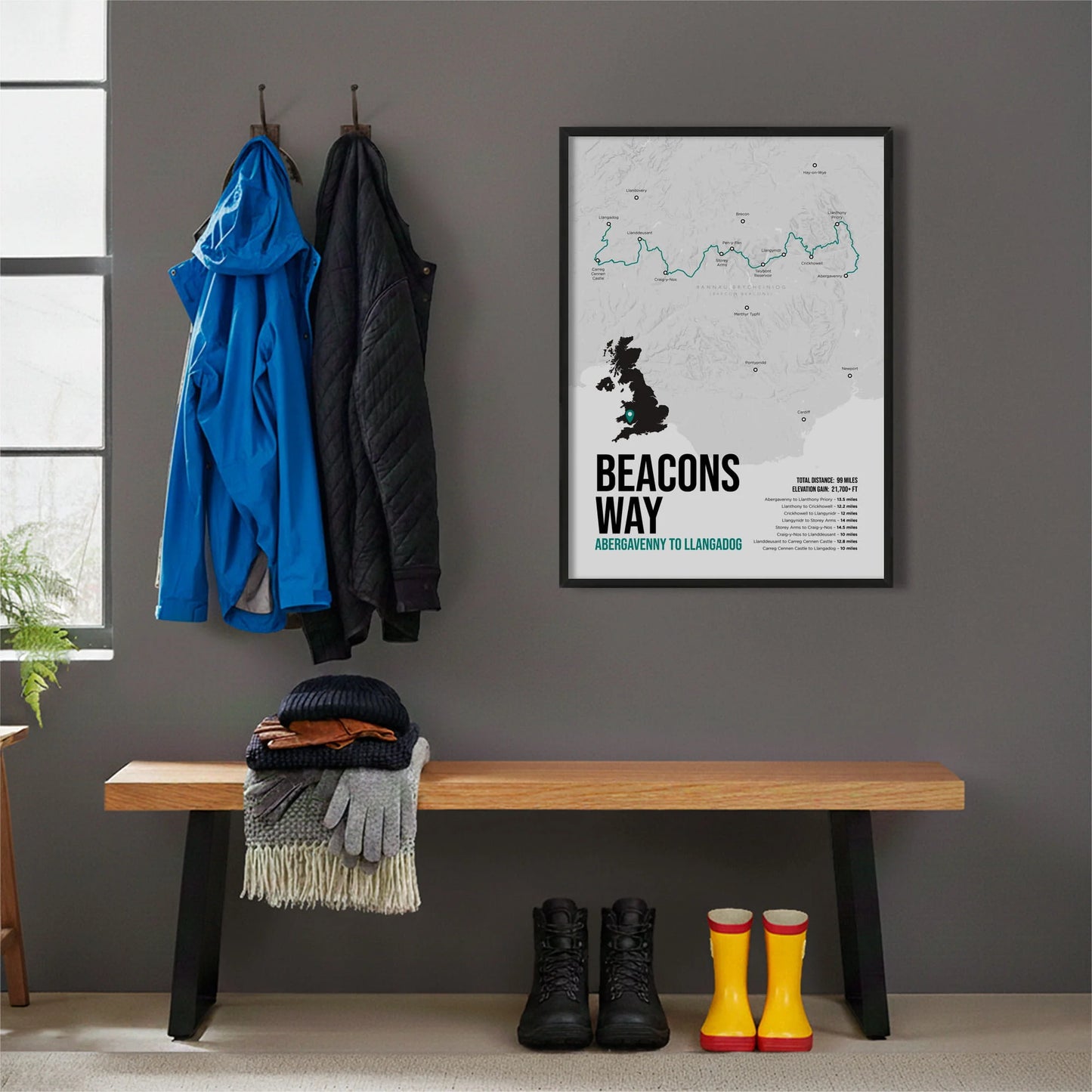 Framed print hanging on grey wall beside coats hanging above bench with walking boots and a scarf