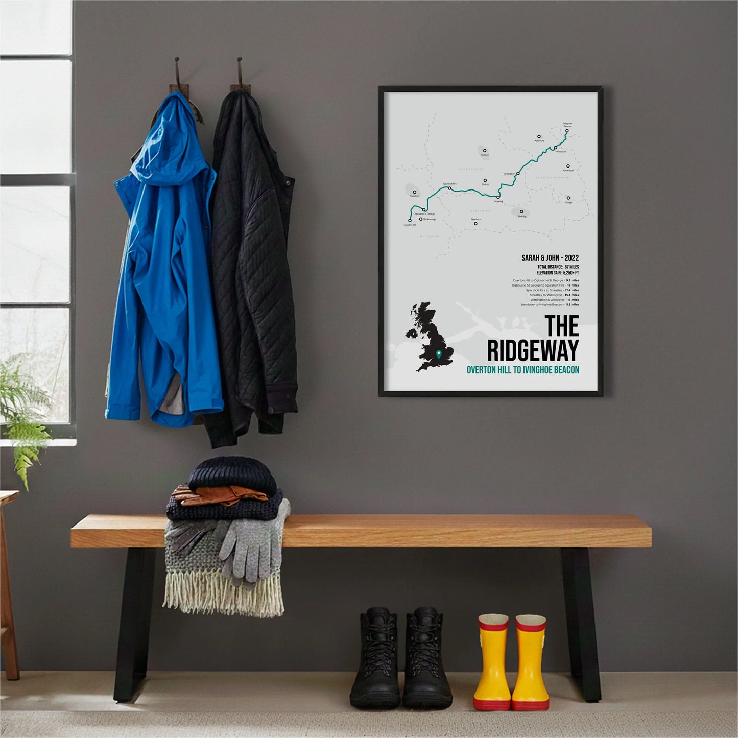 Framed print hanging on grey wall beside coats hanging above bench with walking boots and a scarf