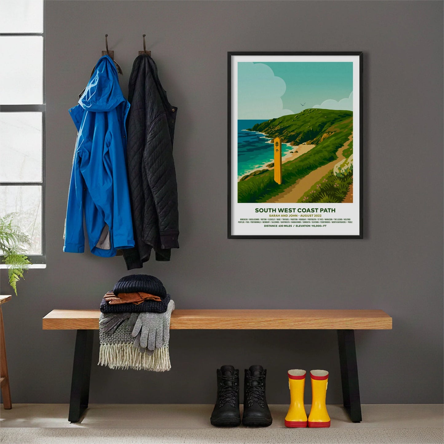 Framed print hanging on grey wall beside coats hanging above bench with walking boots and a scarf