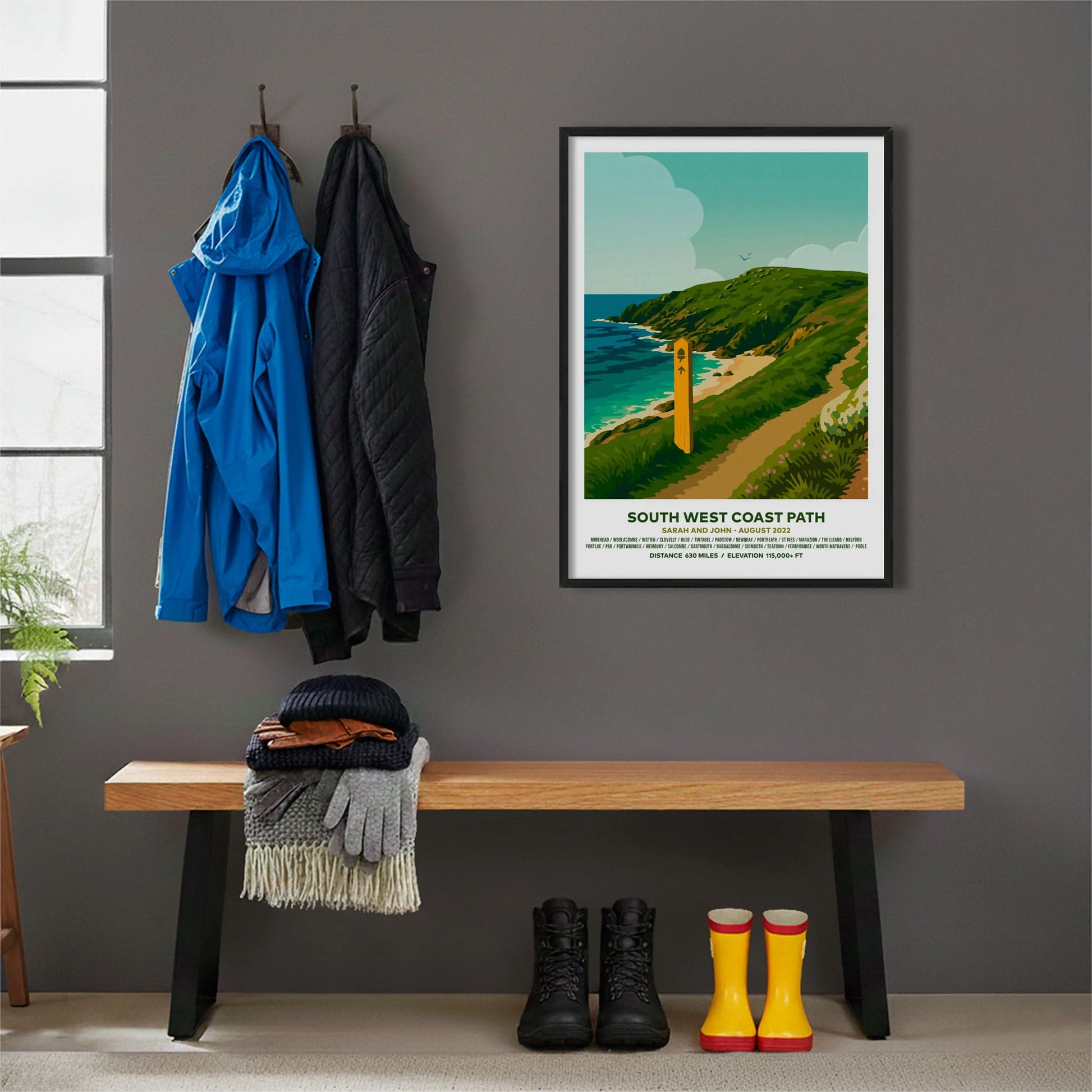 Framed print hanging on grey wall beside coats hanging above bench with walking boots and a scarf