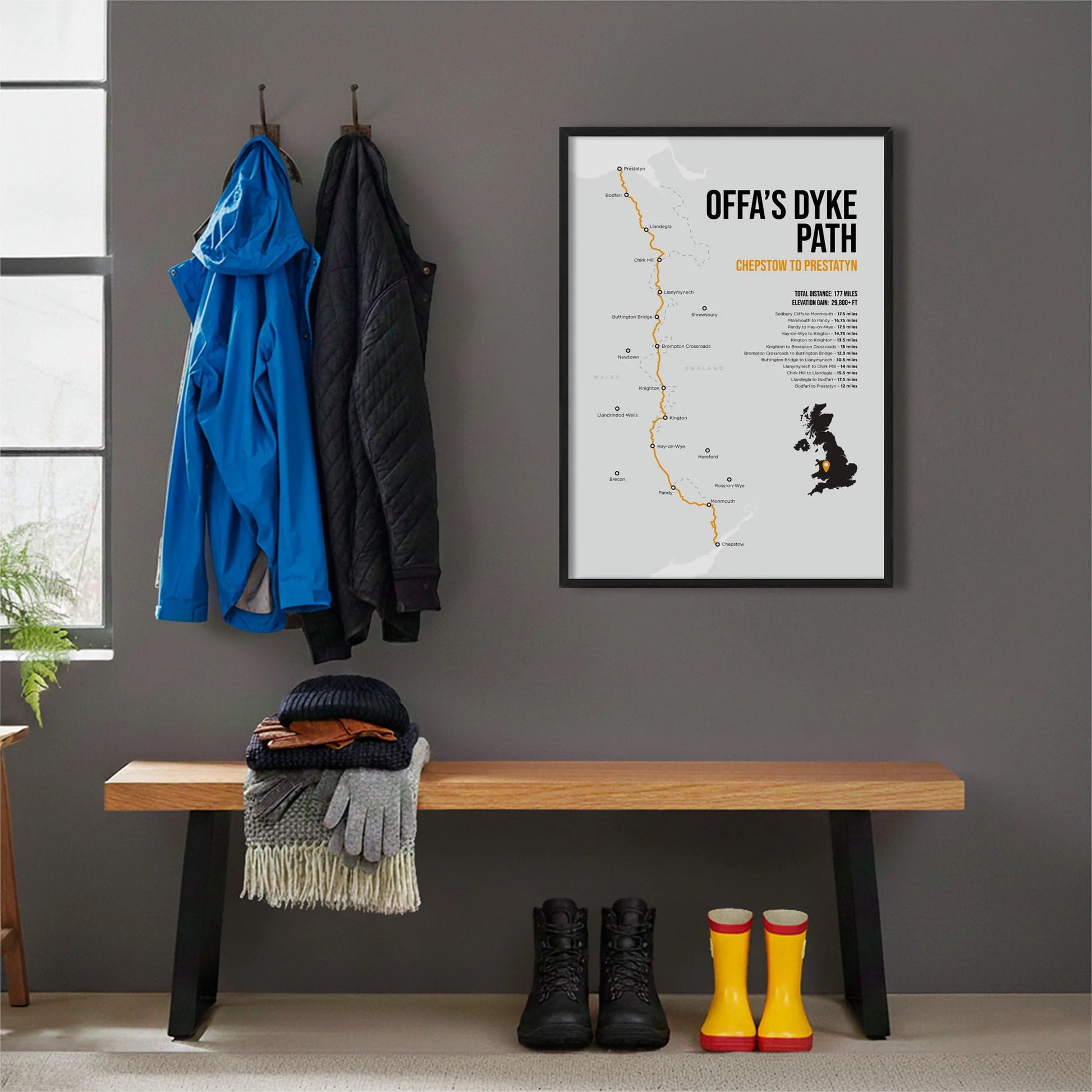 Framed print hanging on grey wall beside coats hanging above bench with walking boots and a scarf
