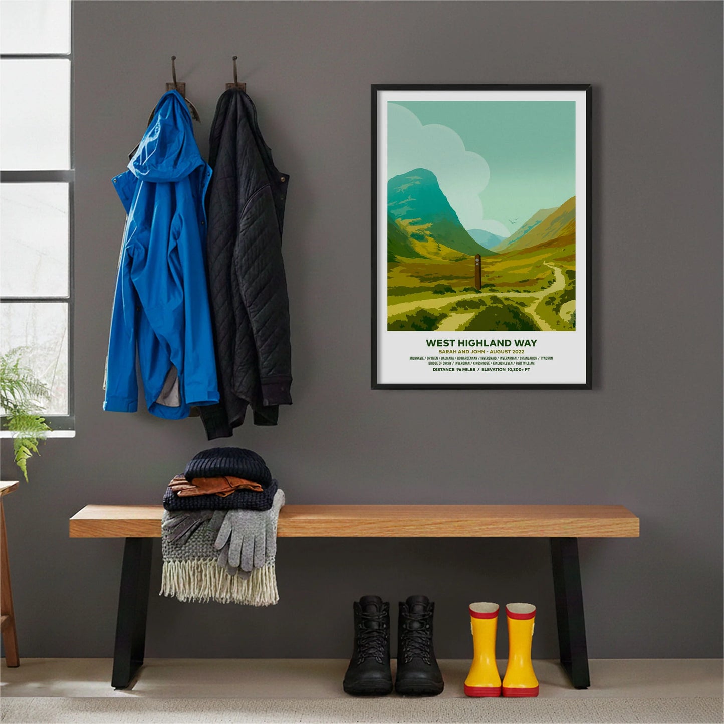Framed print hanging on grey wall beside coats hanging above bench with walking boots and a scarf