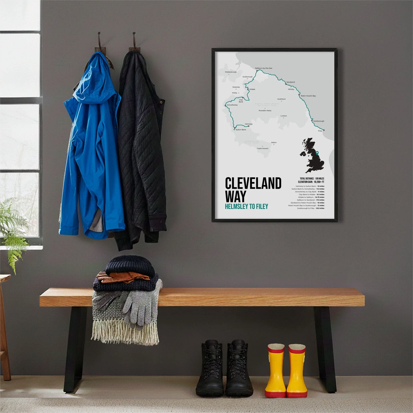 Framed print hanging on grey wall beside coats hanging above bench with walking boots and a scarf