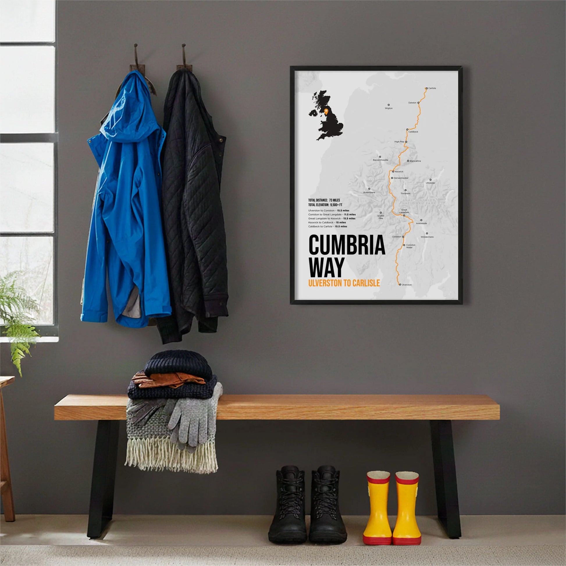 Framed print hanging on grey wall beside coats hanging above bench with walking boots and a scarf