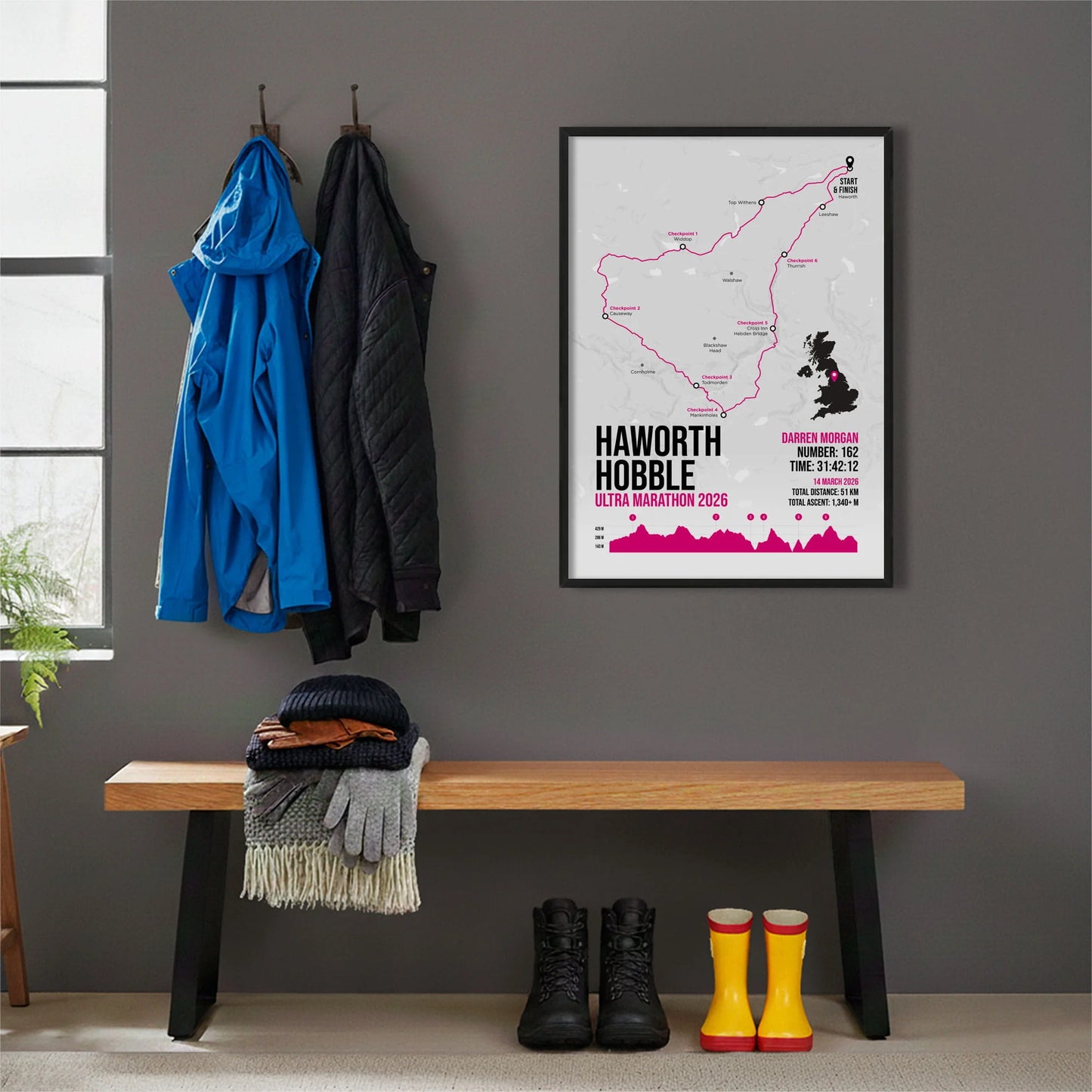 Framed print hanging on grey wall beside coats hanging above bench with walking boots and a scarf