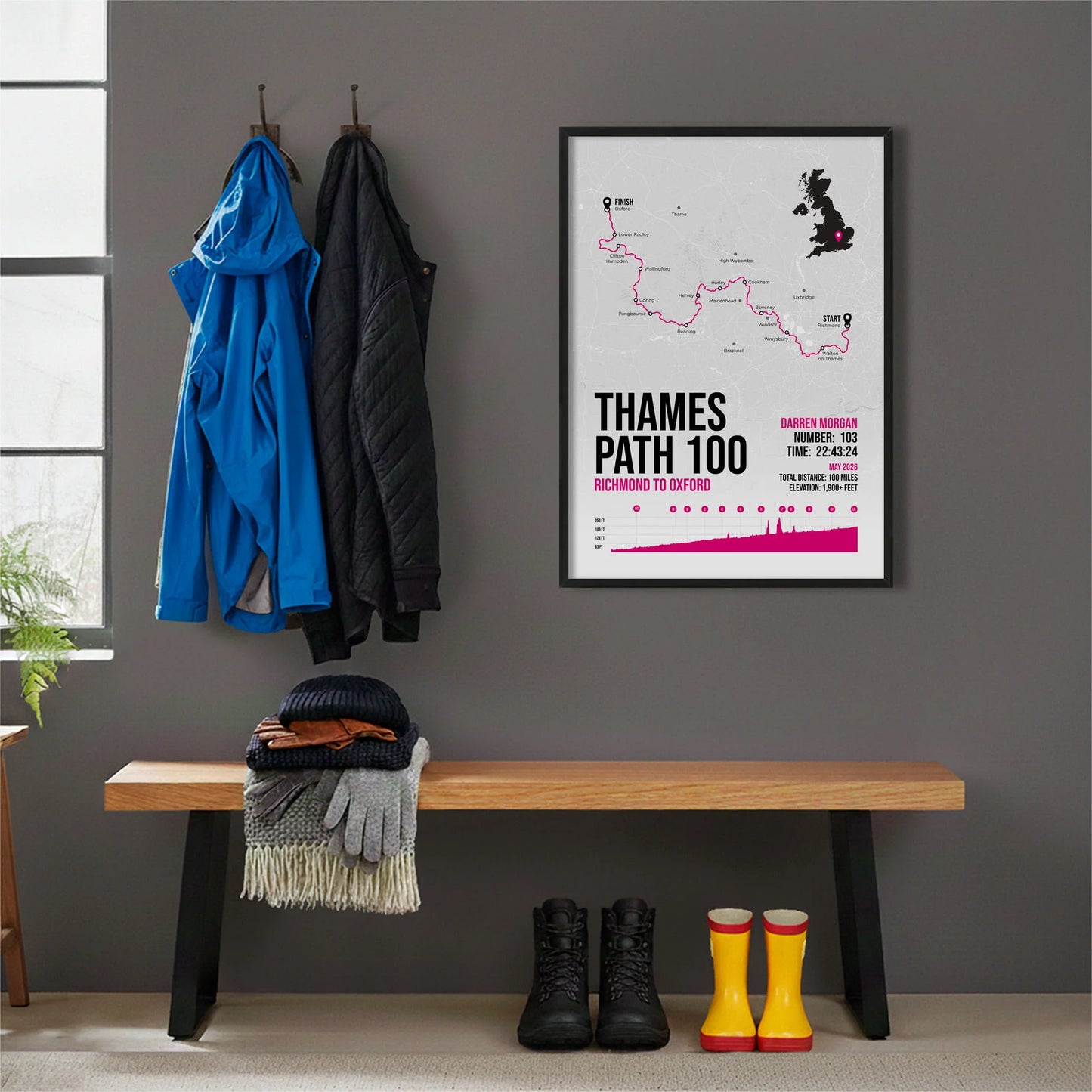 Framed print hanging on grey wall beside coats on hooks above walking boots and shows