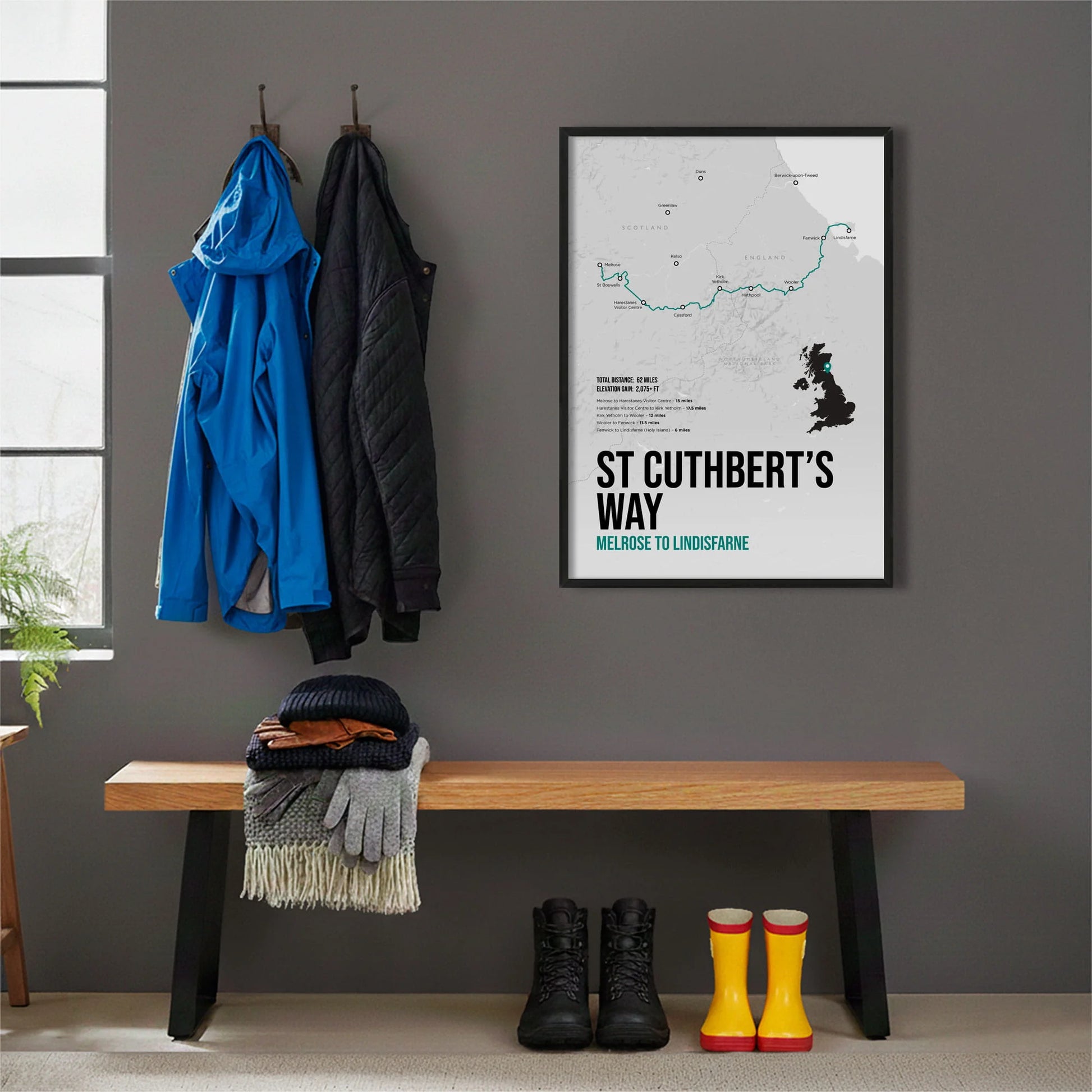 Framed print hanging on grey wall beside coats hanging above bench with walking boots and a scarf
