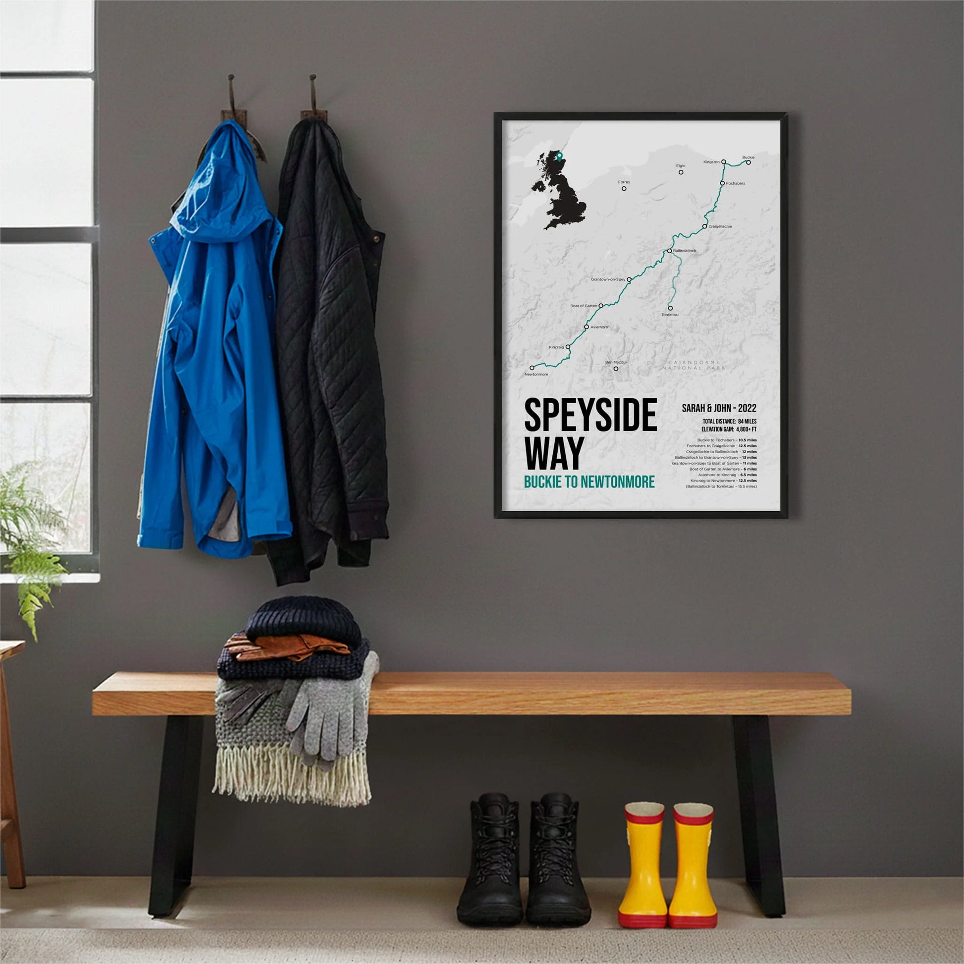 Framed print hanging on grey wall beside coats hanging above bench with walking boots and a scarf